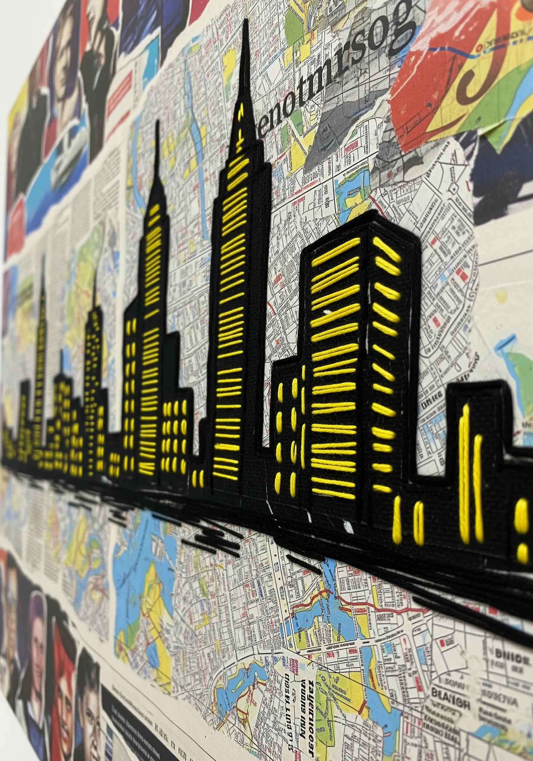 A city skyline in black silhouette stitched with bright yellow satin stitch over a map collage.