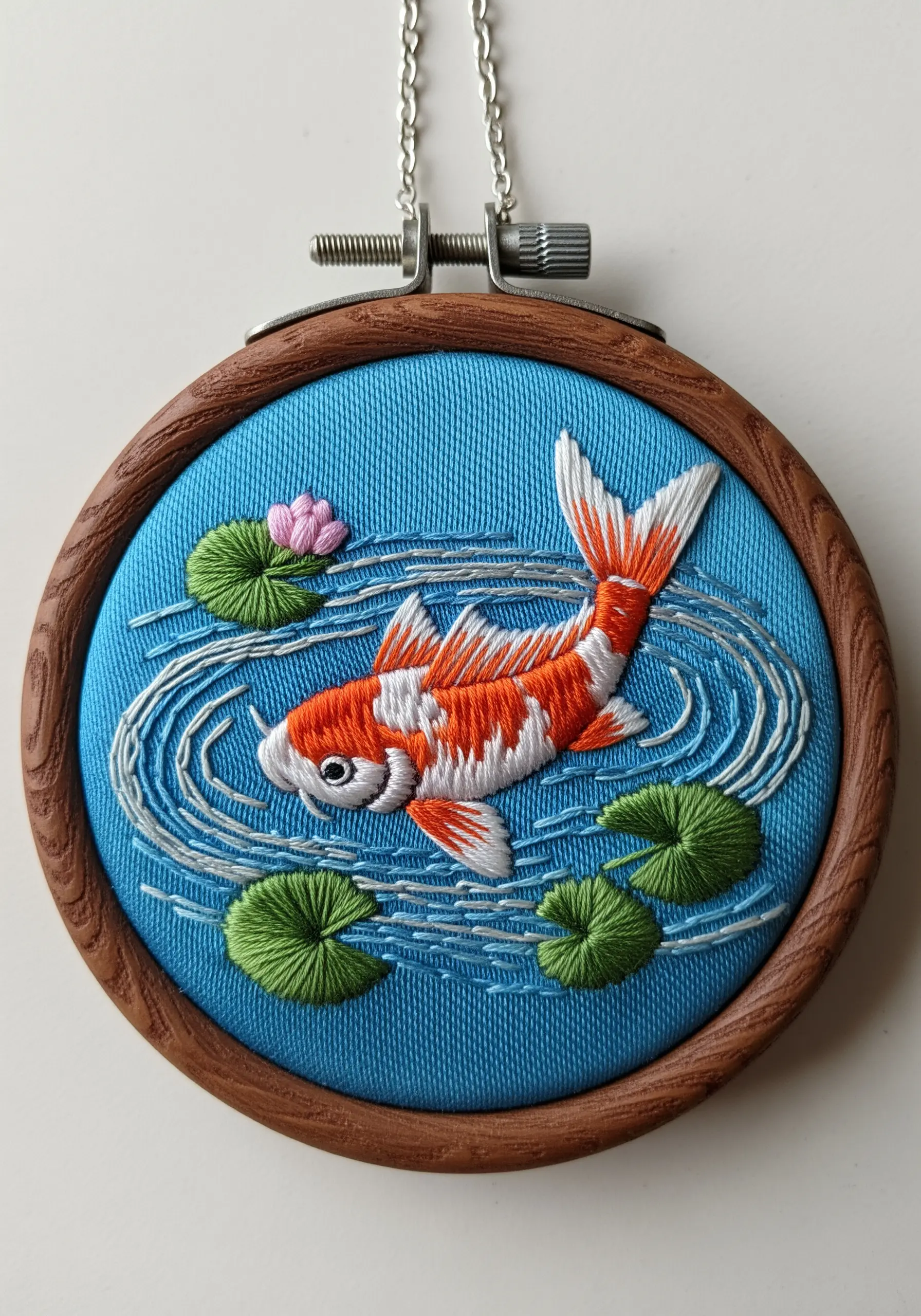 An embroidered koi fish in a pond with stitched water ripples and lily pads.