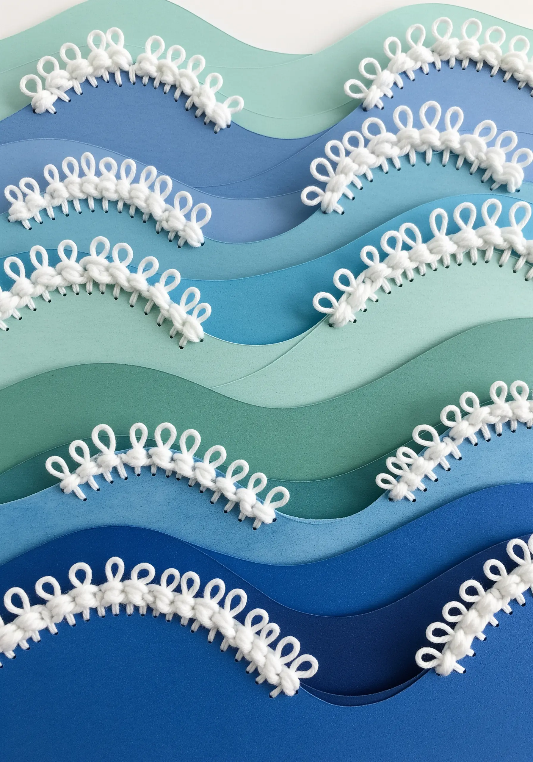 Layered blue paper waves topped with white, loopy embroidered stitches that mimic sea foam.