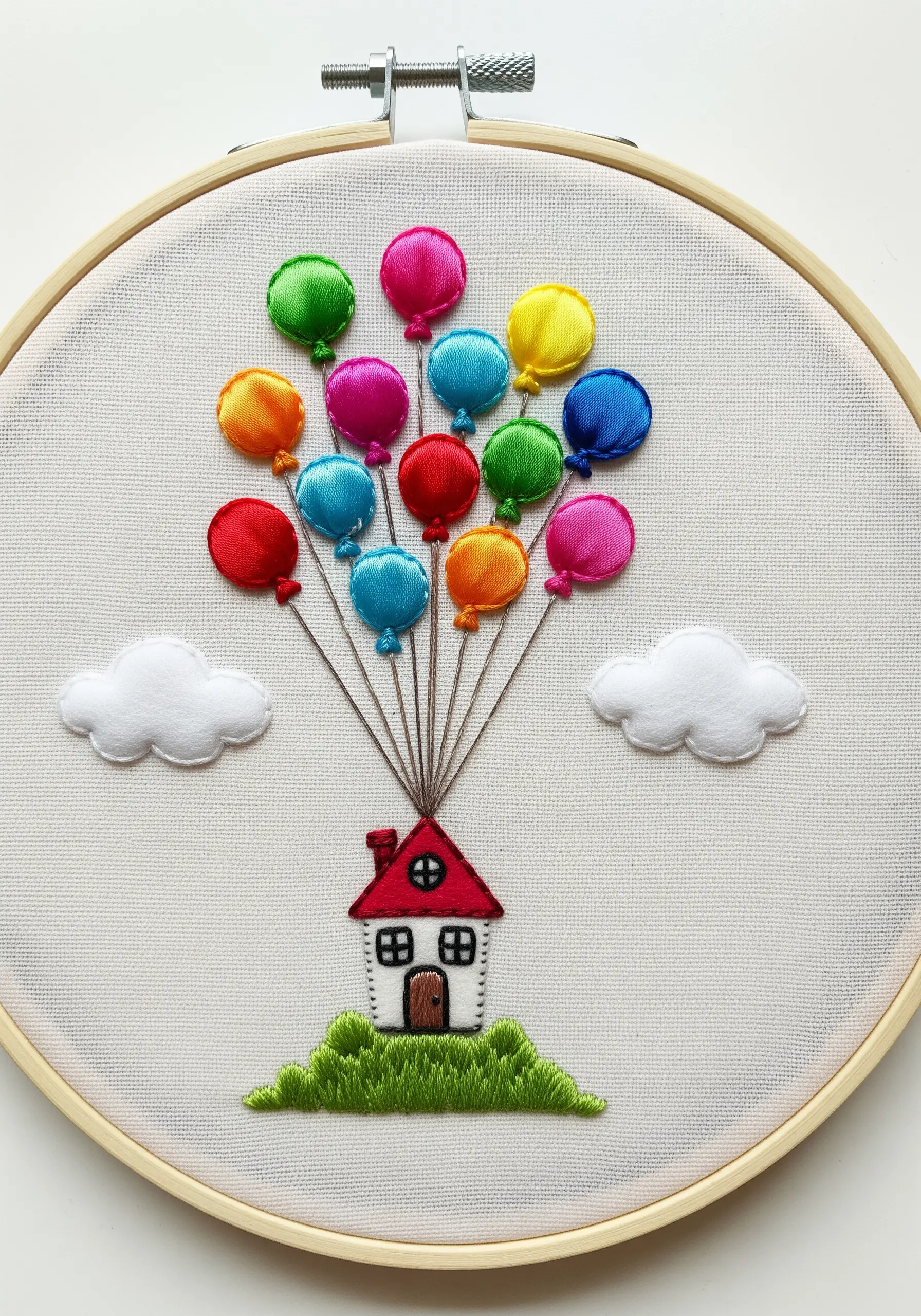 Embroidery hoop art of a house being lifted by colorful, 3D satin appliqué balloons.