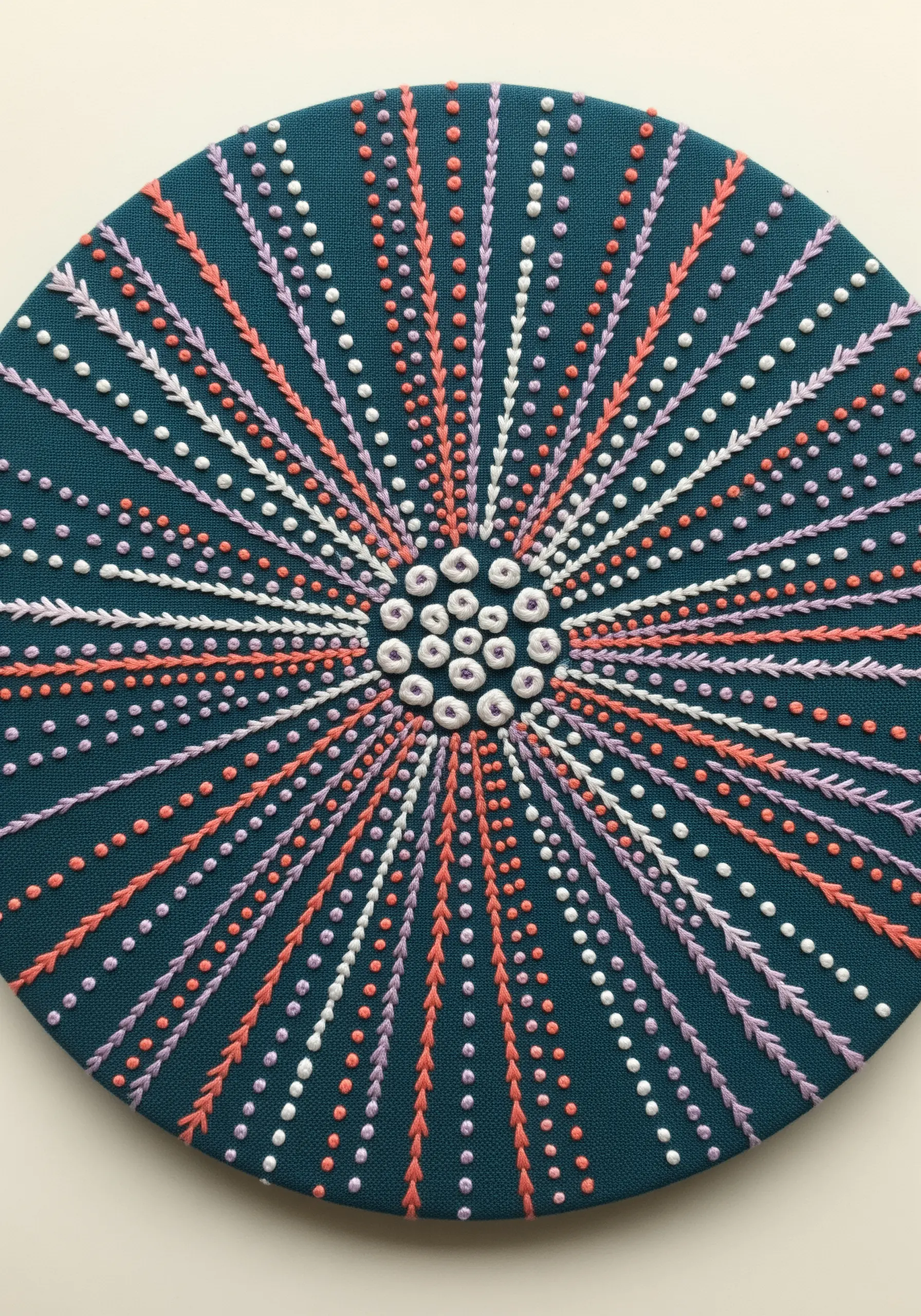Abstract sea urchin embroidery with radial patterns of French knots and fly stitches.