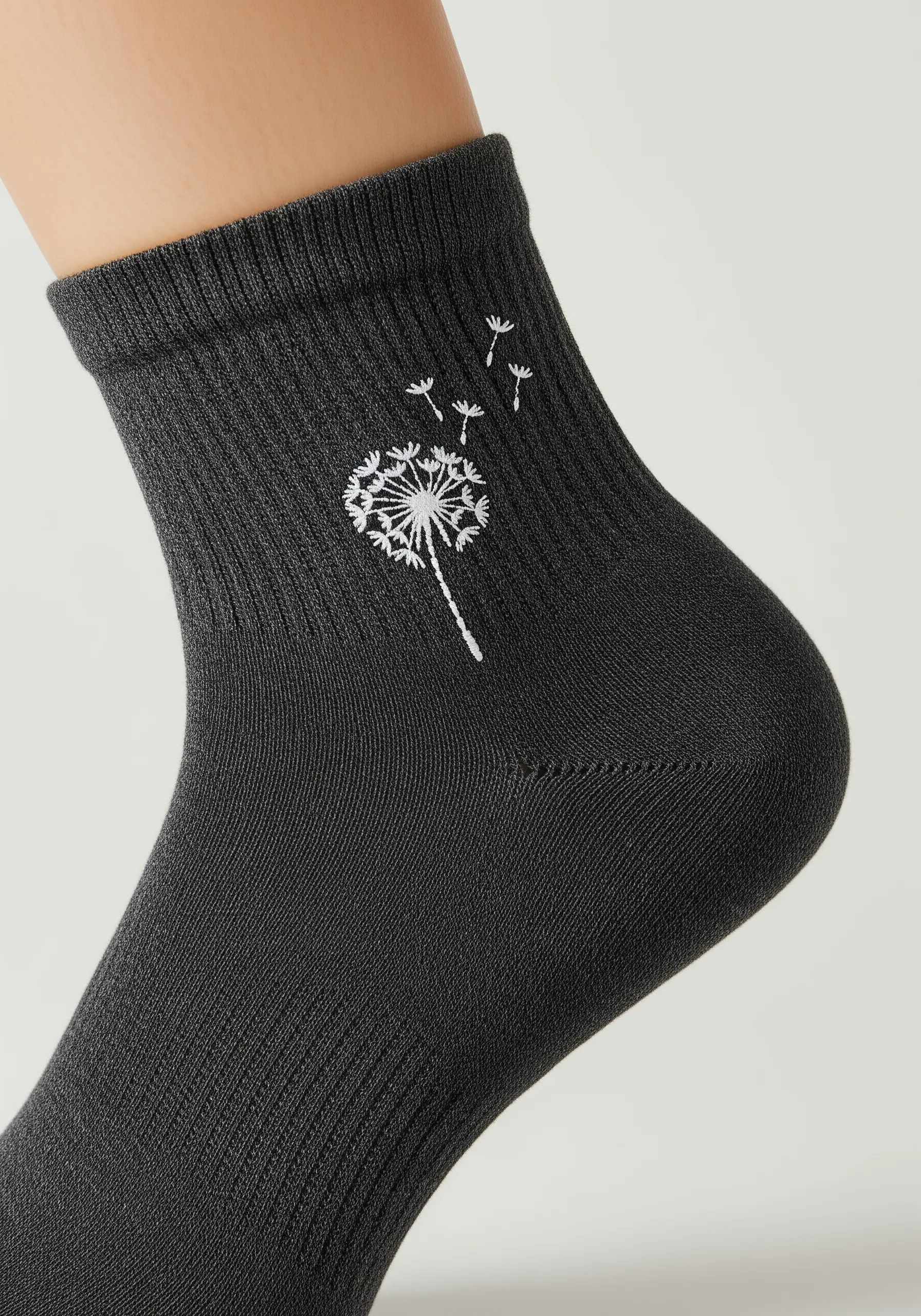 A white embroidered dandelion with seeds blowing away on a dark grey sock.
