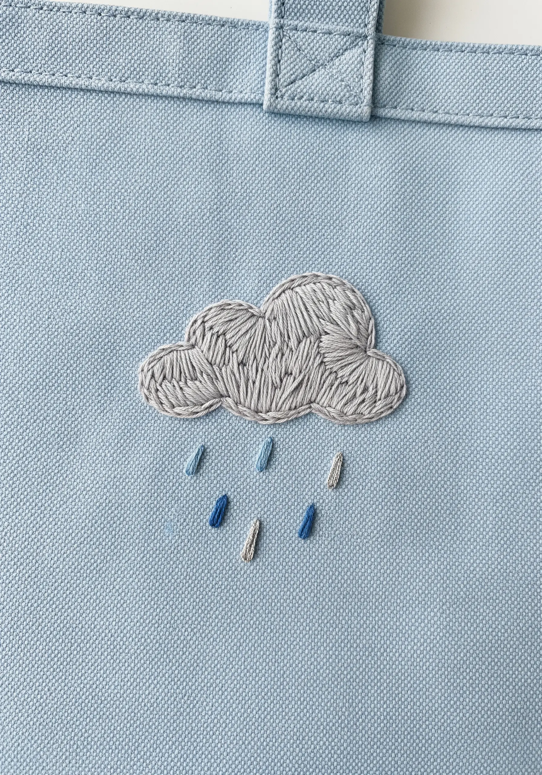 A grey embroidered cloud with a textured fill, with blue variegated raindrops.