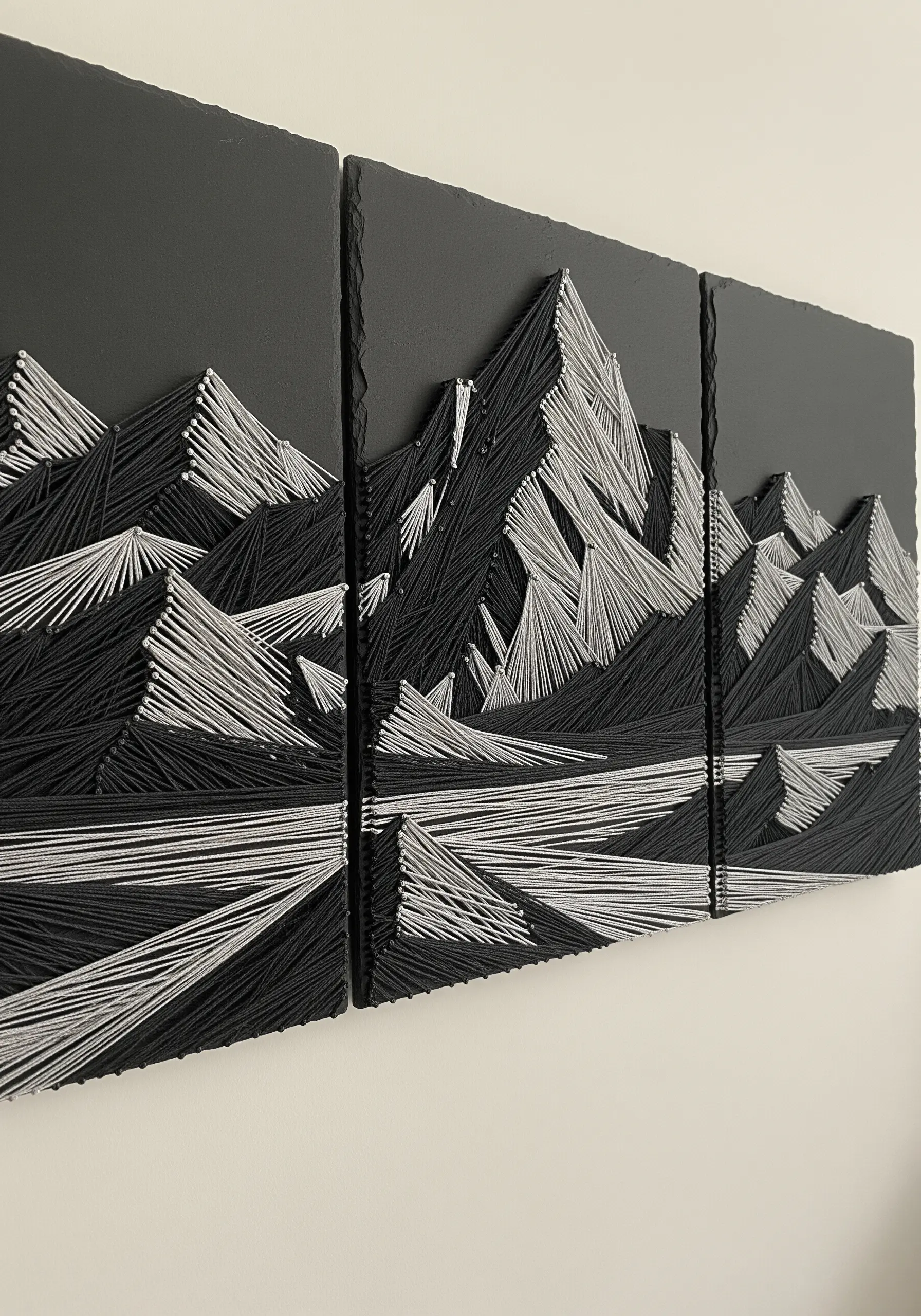 A black and white string art triptych of a dramatic mountain range.