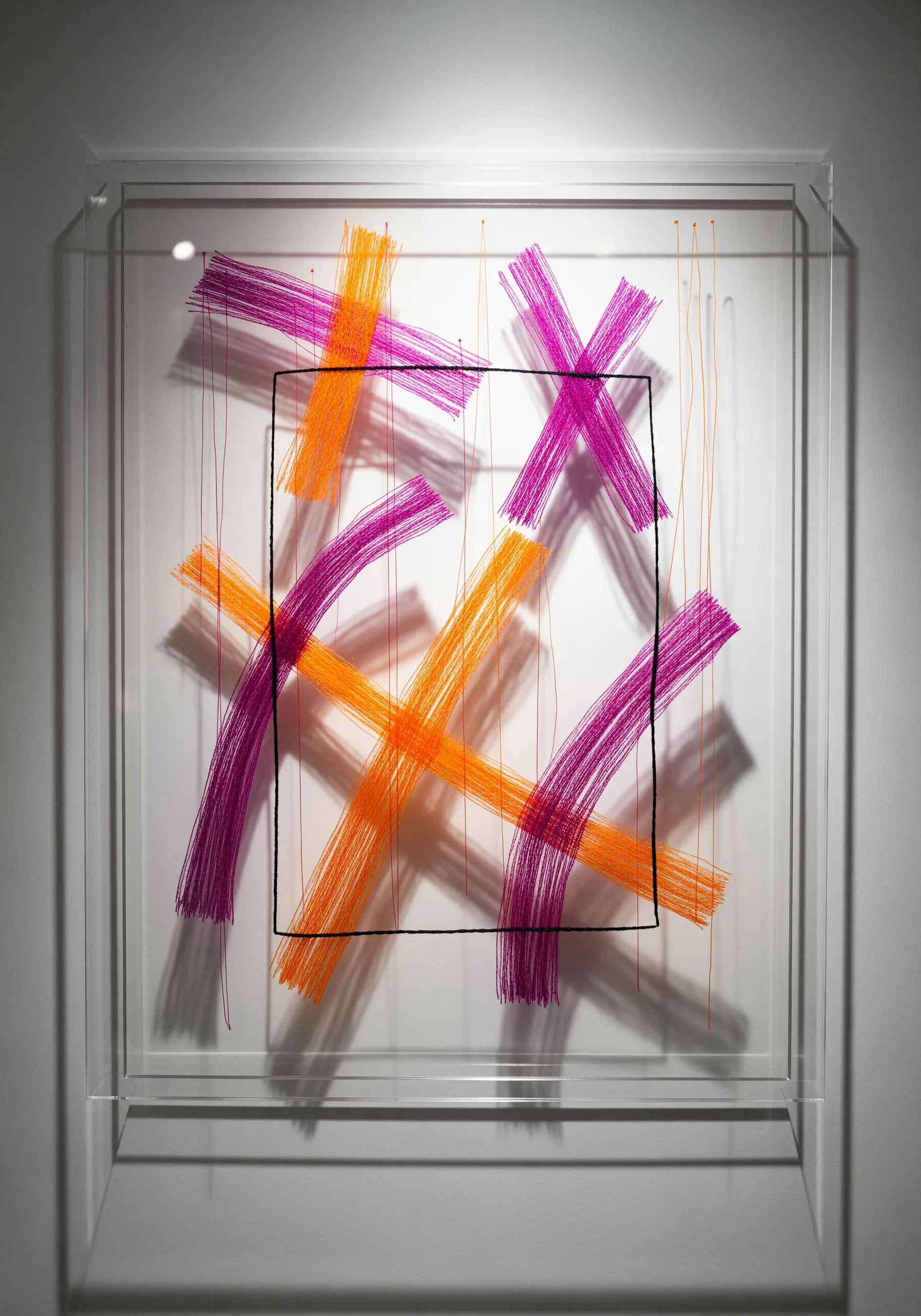 Abstract art with orange and magenta threads stretched across a clear acrylic box.