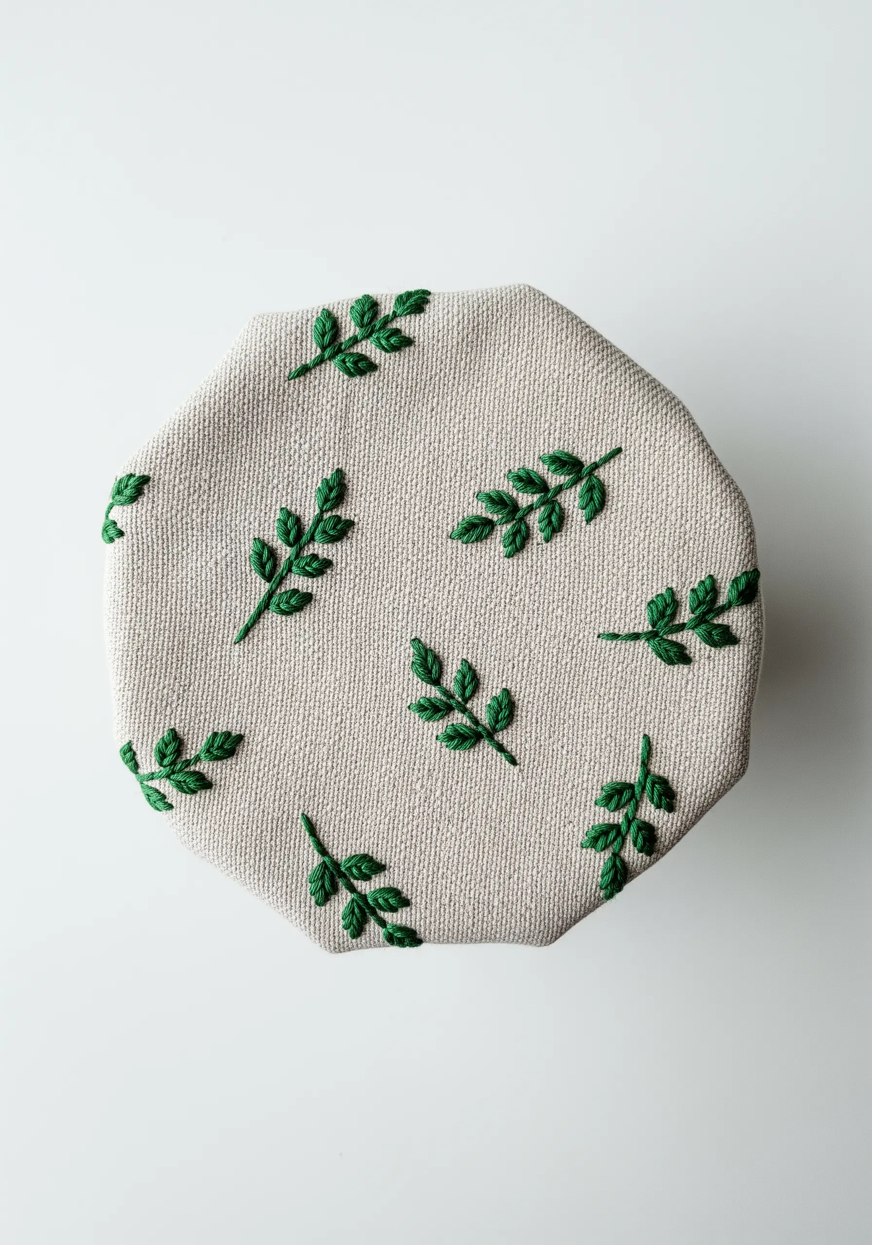 A fabric jar cover embroidered with a scattered pattern of small green leaves.