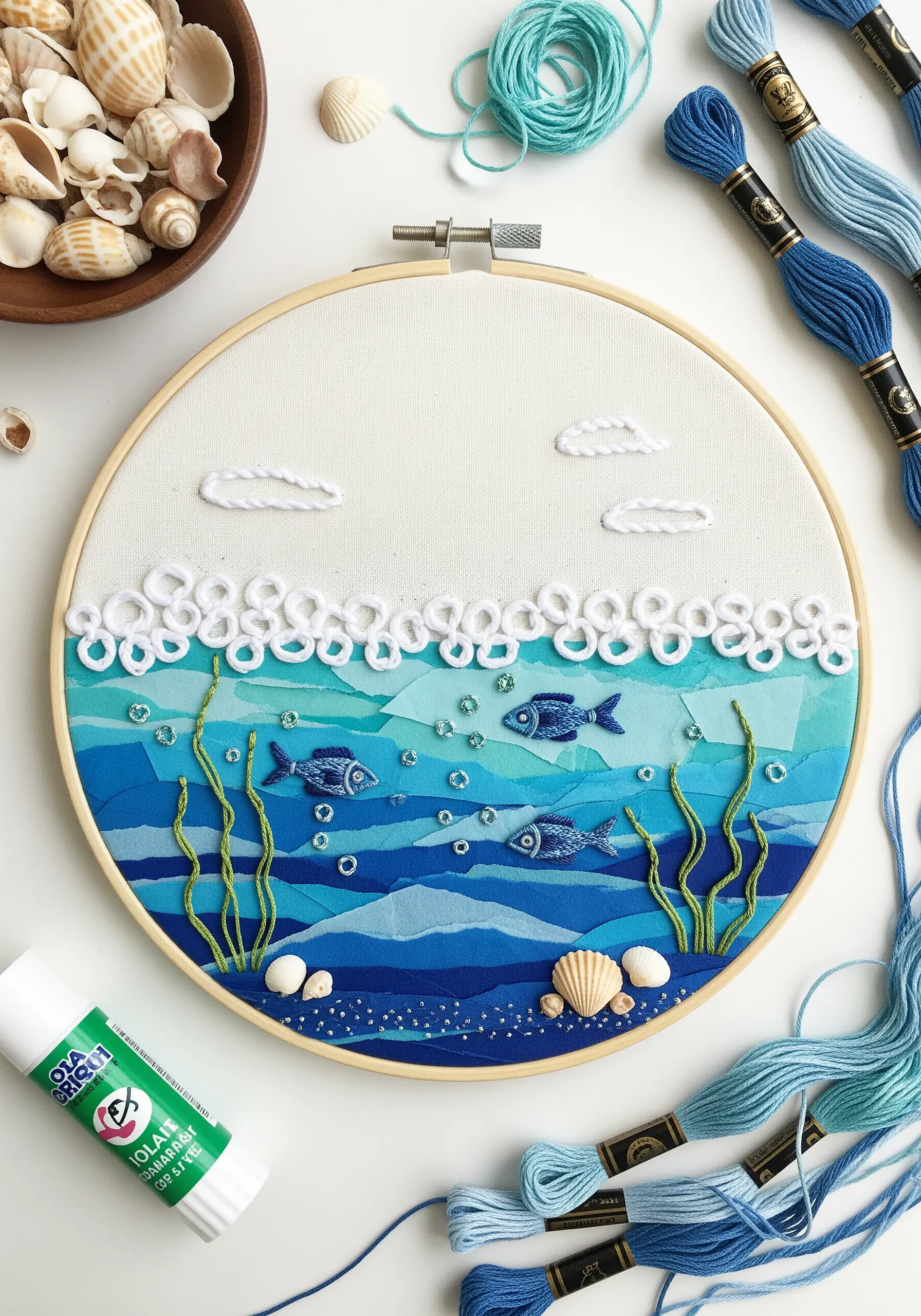 Ocean scene in a hoop with layered blue fabric collage, white thread bubbles, and stitched fish.