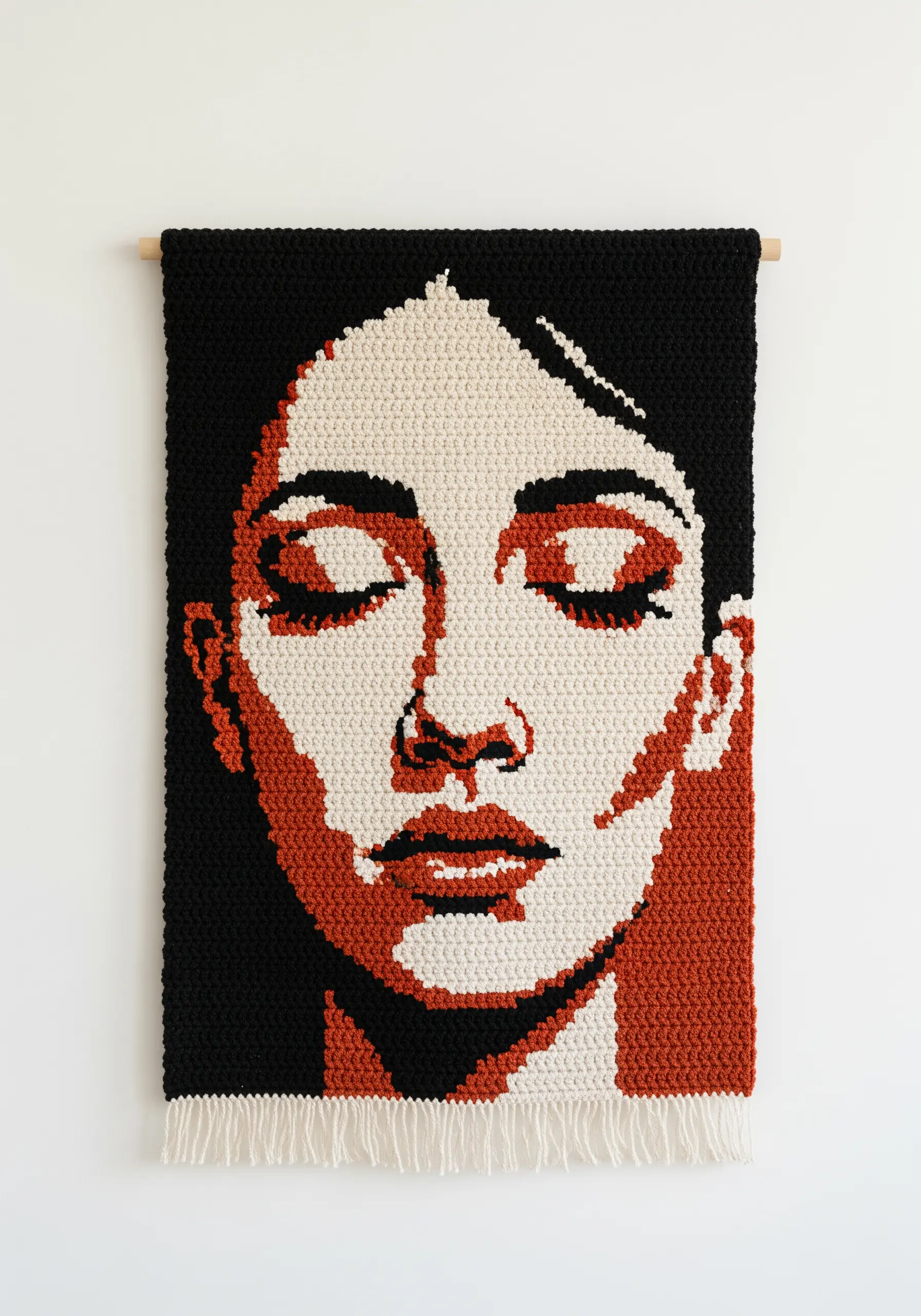 A crocheted wall hanging depicting a woman's face in a high-contrast graphic style.
