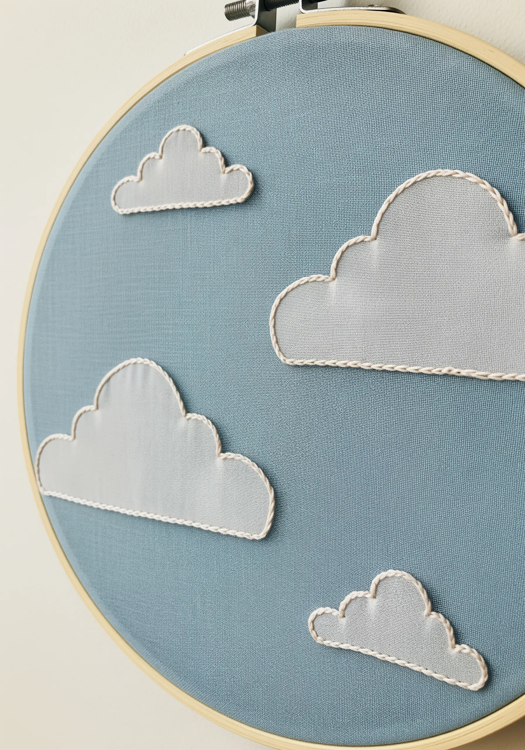 Appliqué clouds made from sheer fabric outlined with simple stitches on a blue background.