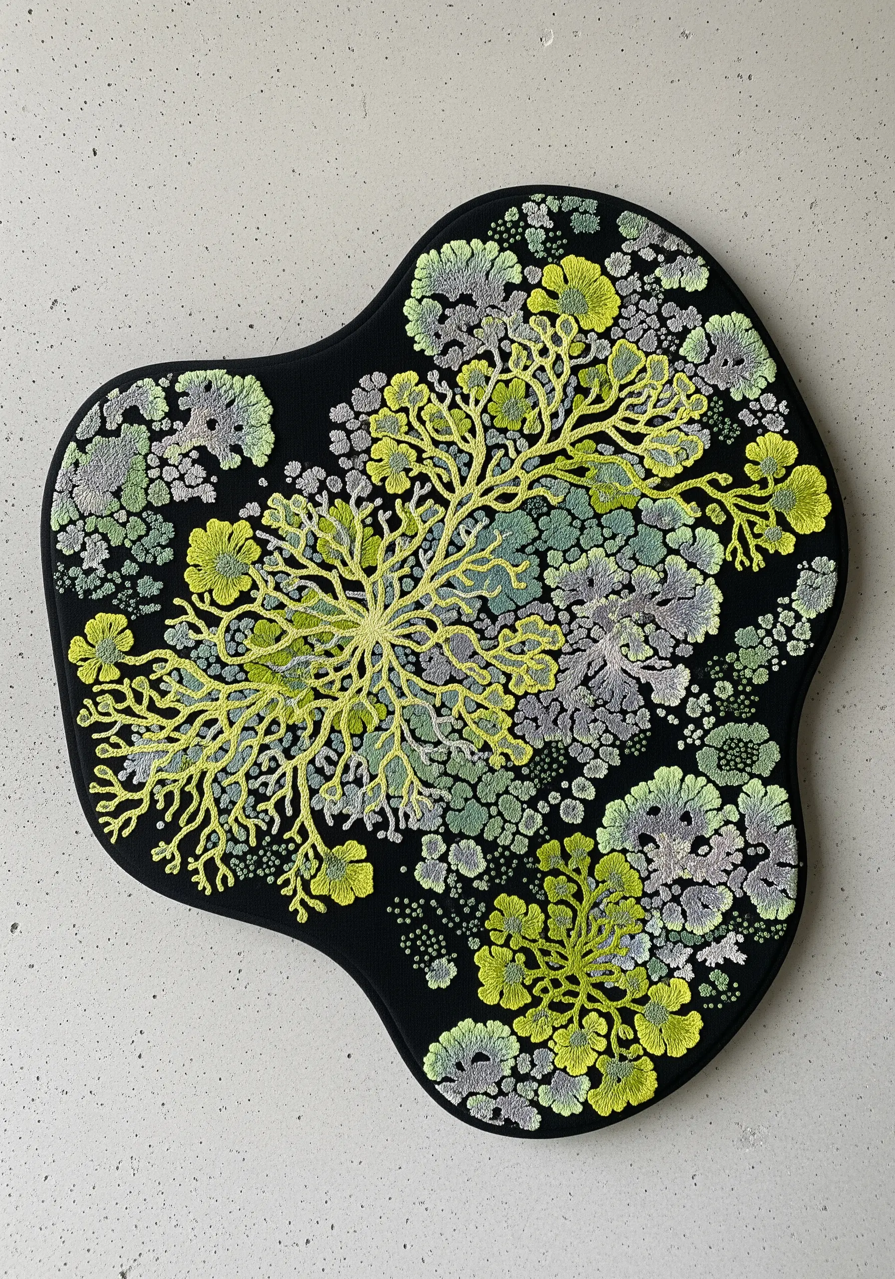An abstract embroidery of lichen in greens and greys, mounted on an irregular, organic-shaped frame.