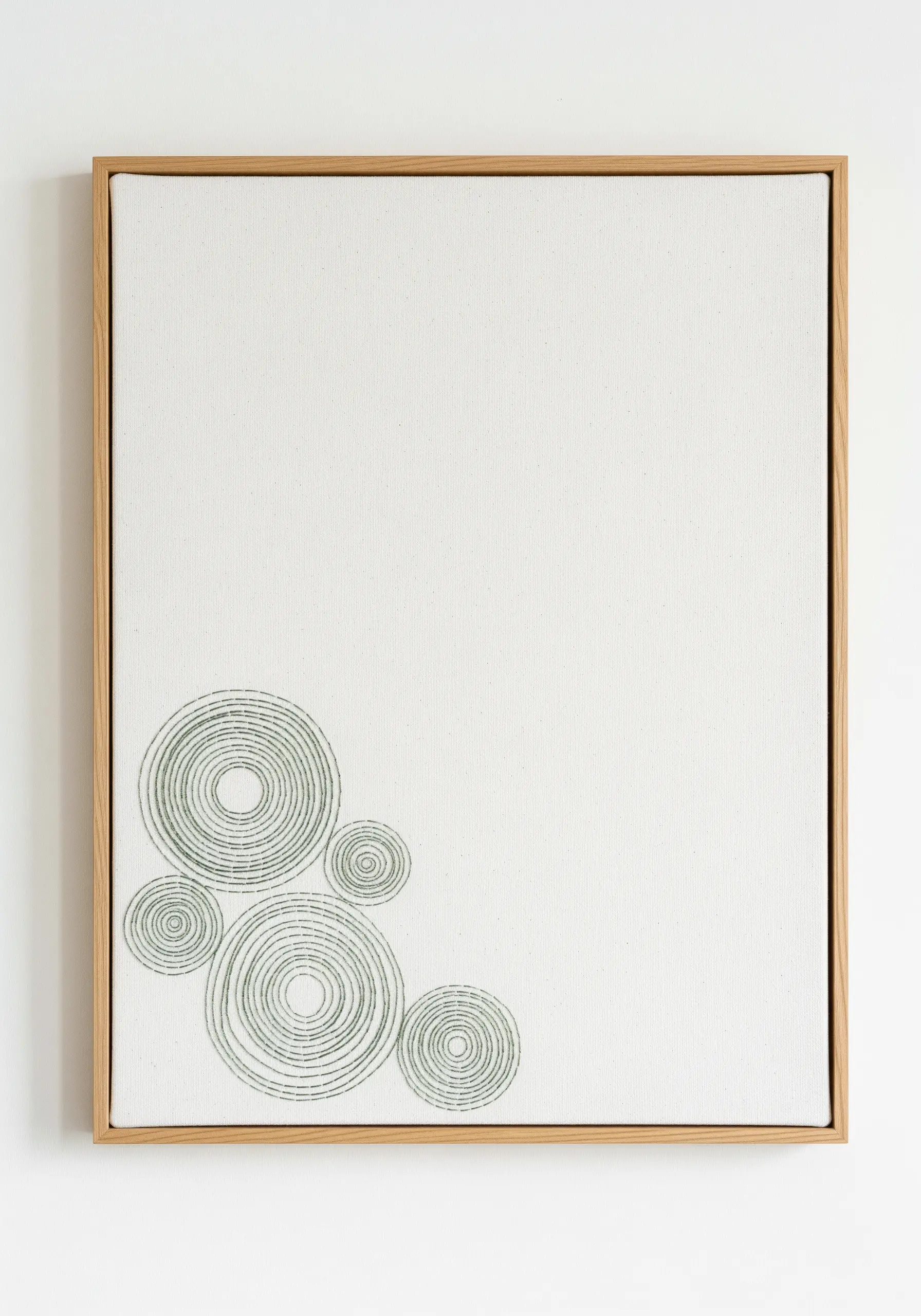 Concentric circles stitched with sage green thread in the corner of a white canvas.