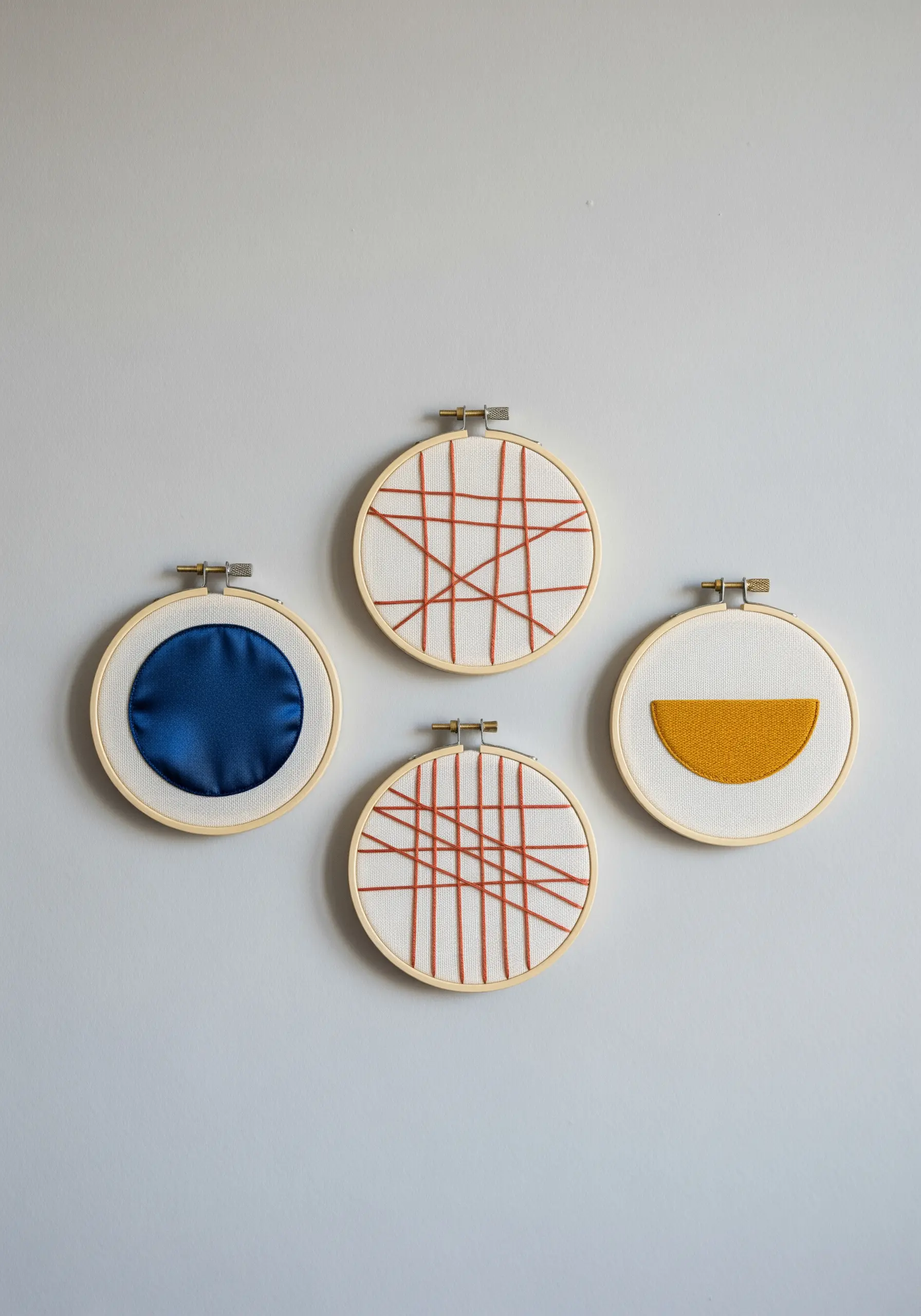 A collection of four embroidery hoops with abstract geometric designs in blue, yellow, and rust.