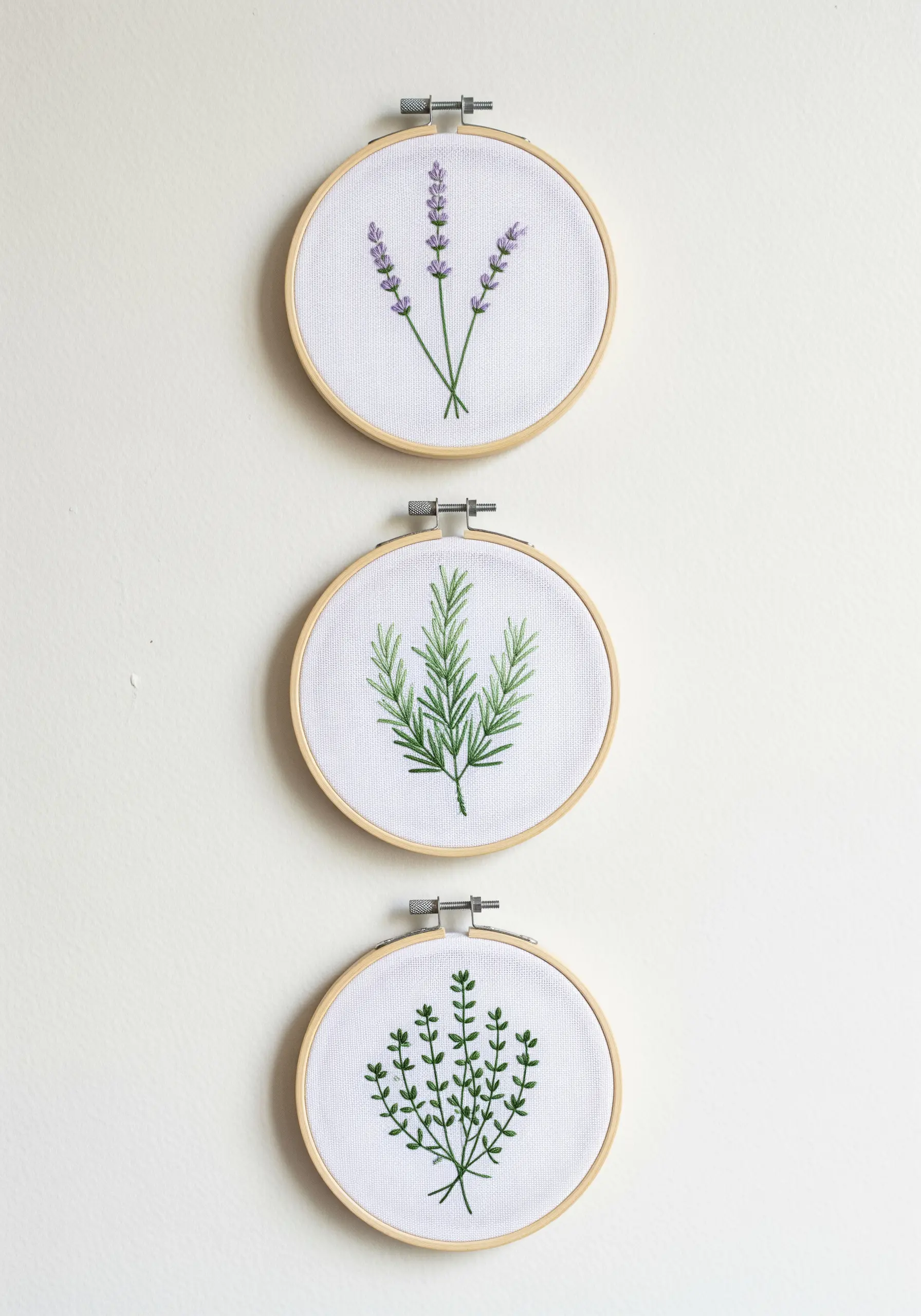 A set of three small embroidery hoops with lavender, rosemary, and thyme.