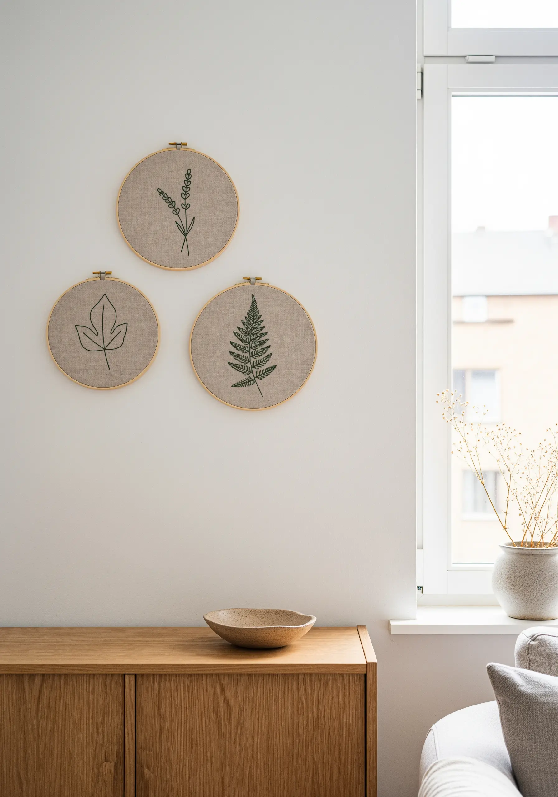 Three embroidery hoops with minimal botanical line art on a neutral wall