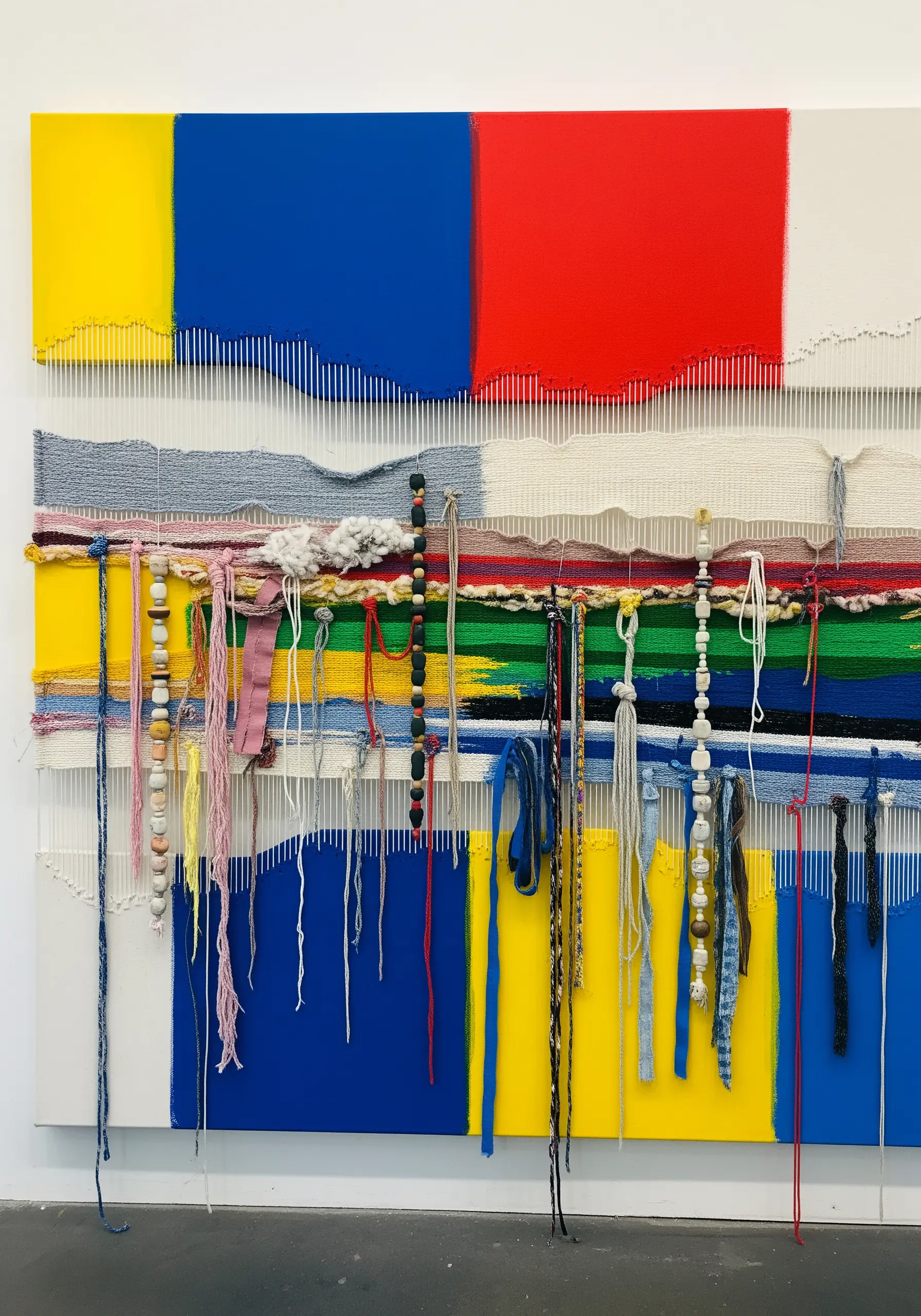 A deconstructed weaving on a color-blocked canvas with loose threads and incorporated beads.