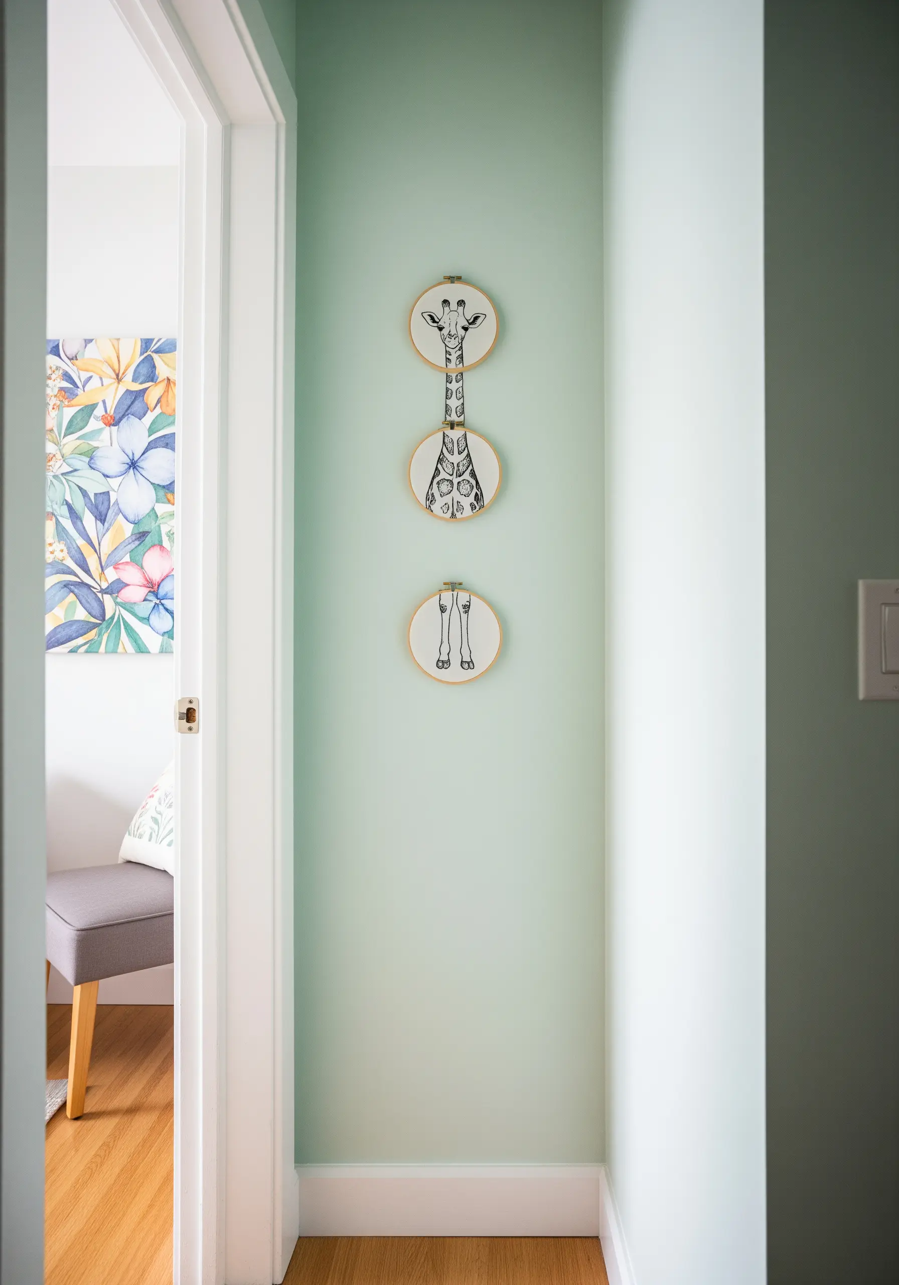 A giraffe embroidered across three separate hoops, stacked vertically on a pale green wall to show its full height.