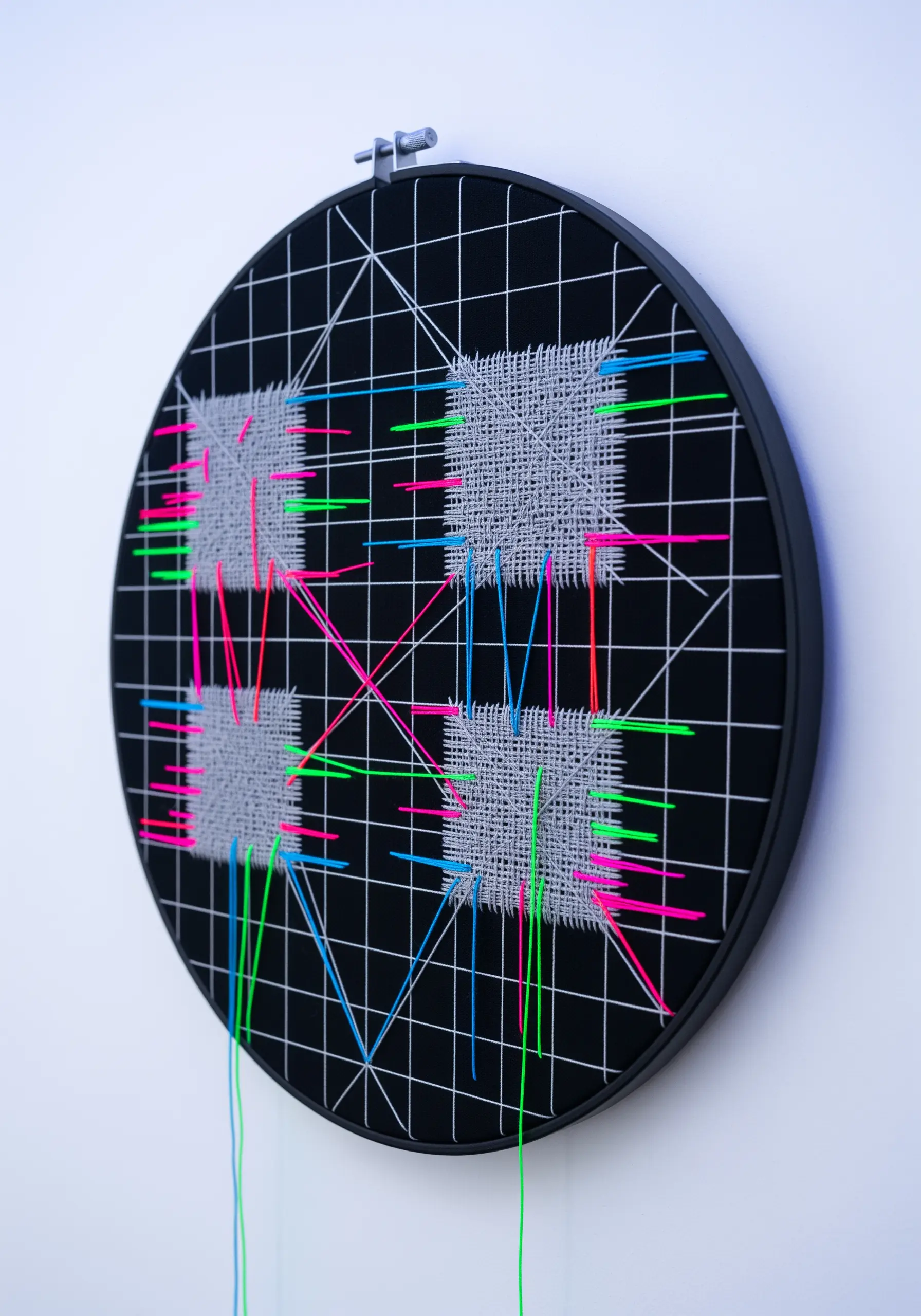 A stitched grid on black fabric with woven gray squares and intersecting neon threads.