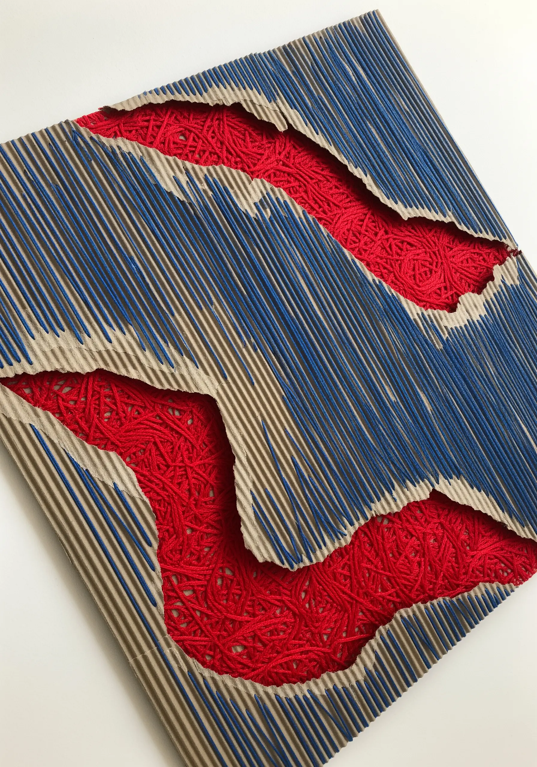 Abstract art with red thread stitched and wrapped through torn corrugated cardboard.