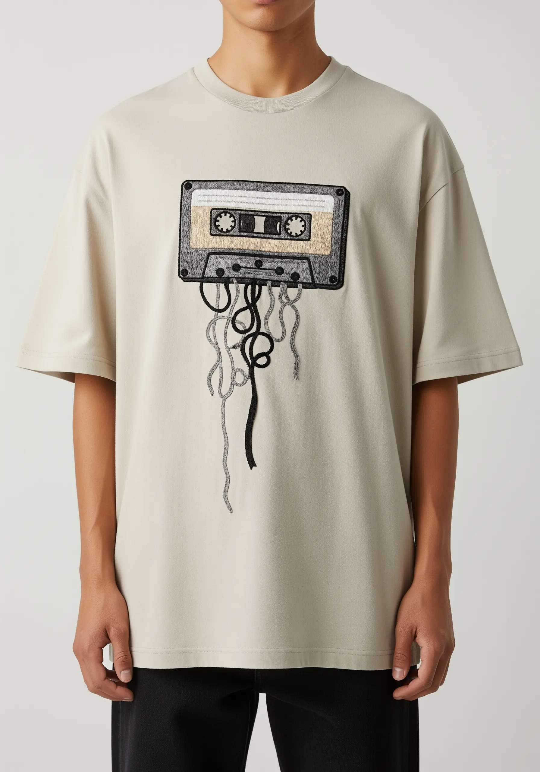 Embroidered cassette tape with threads unspooling and hanging down the front of the t-shirt.