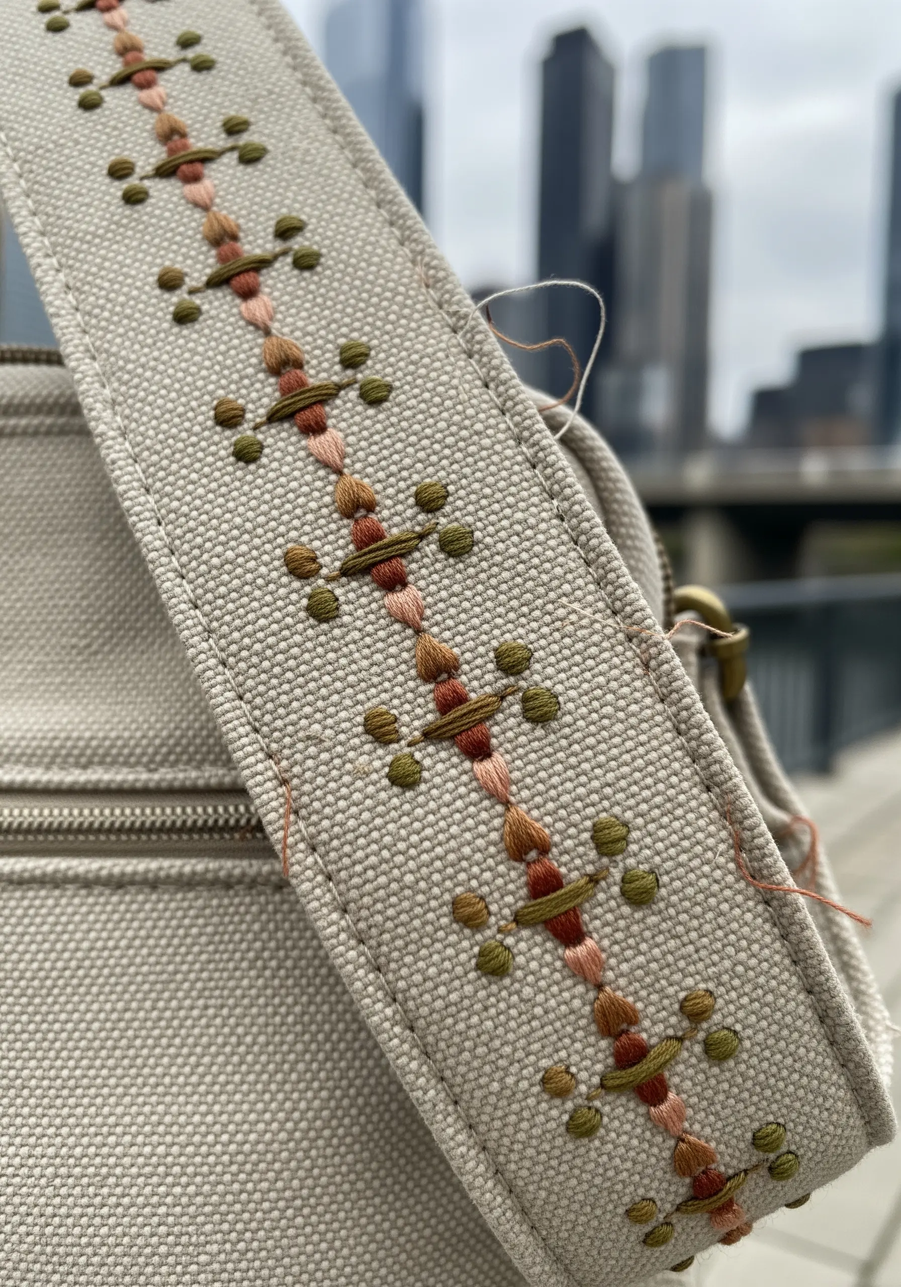 A geometric pattern of French knots and satin stitches in earthy tones on a canvas bag strap.
