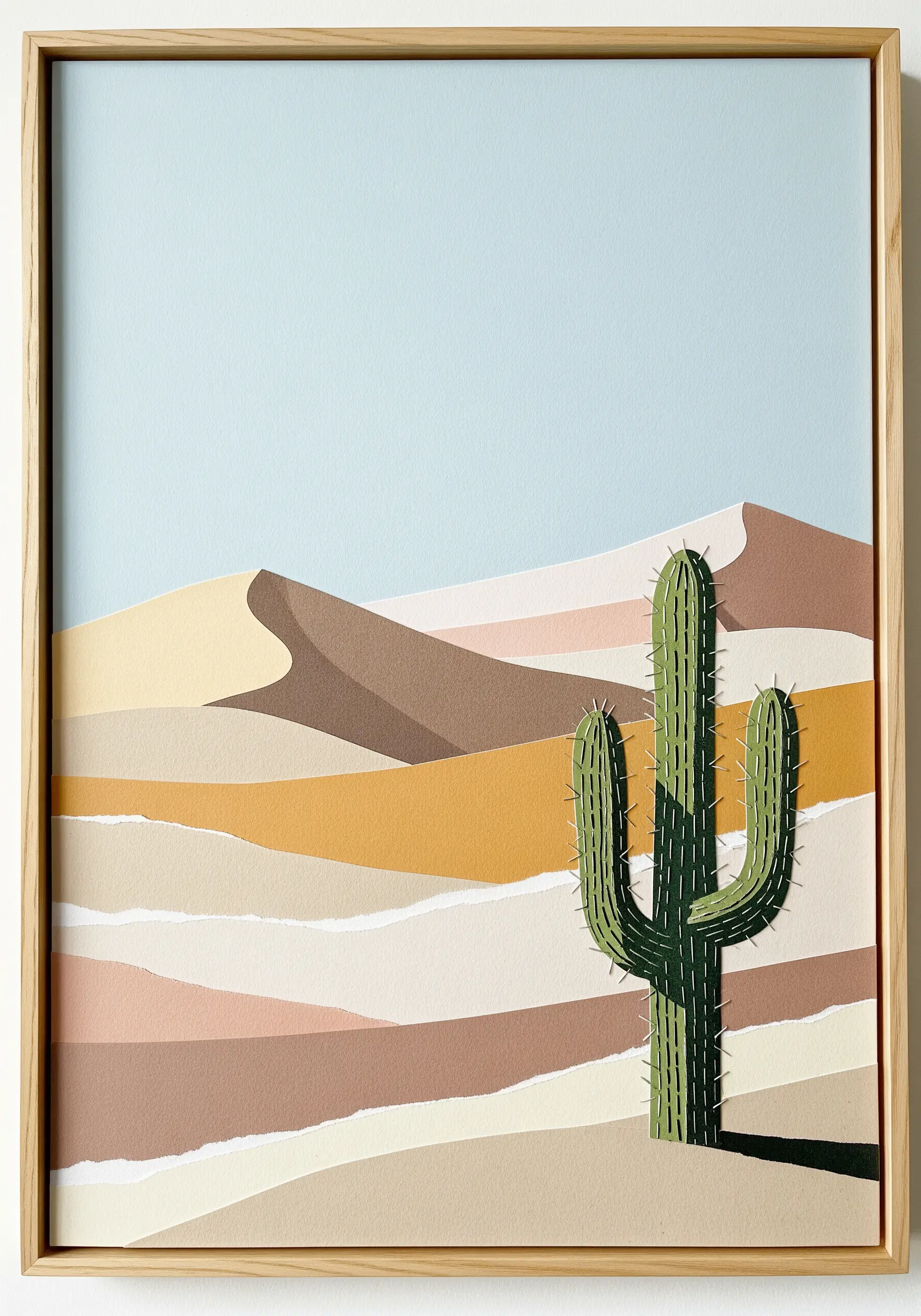 A minimalist desert collage with a paper cactus that is outlined and detailed with green embroidery.