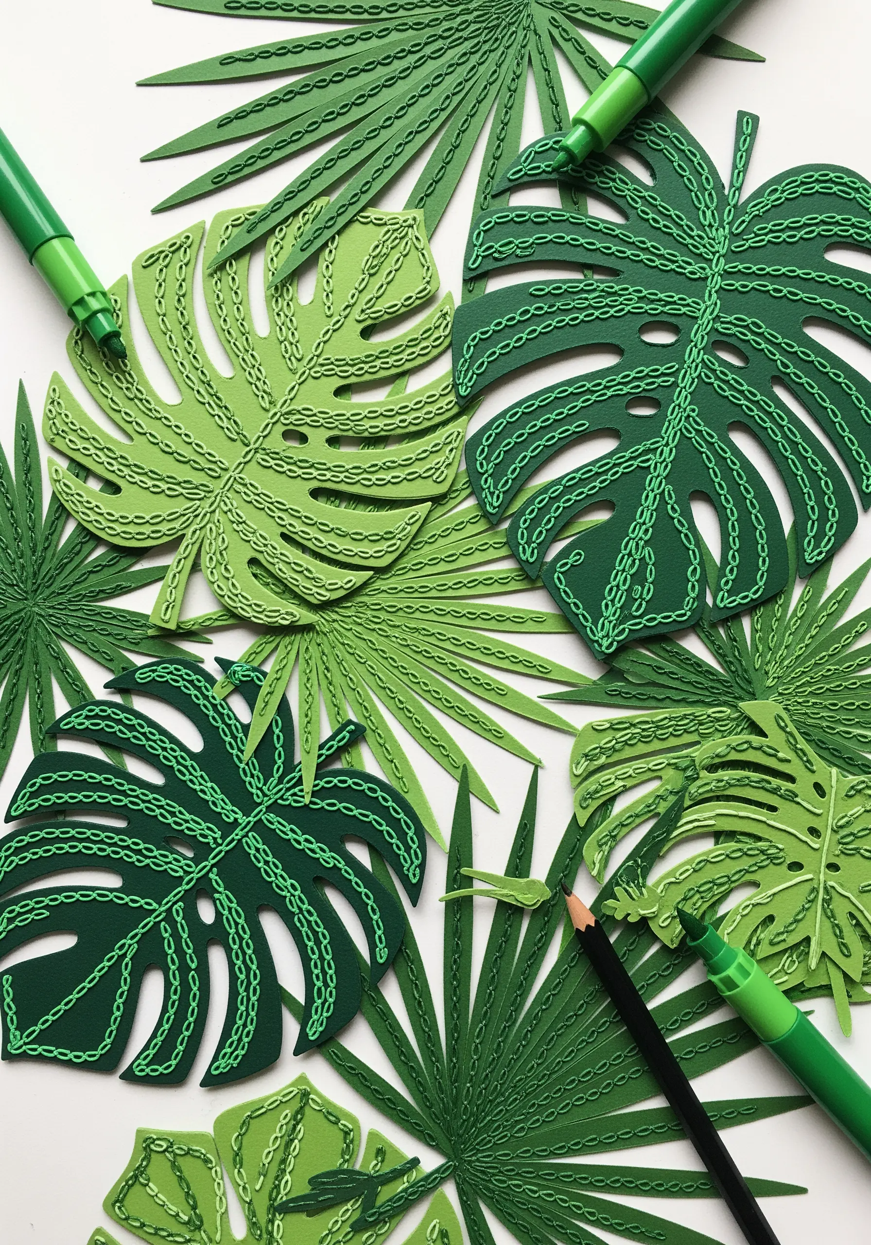 Green paper monstera and palm leaves decorated with hand-drawn chain stitch patterns.
