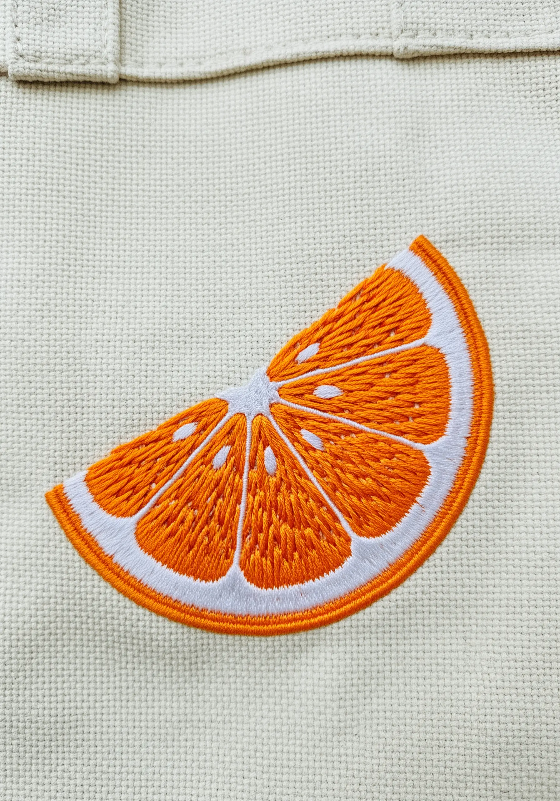 An embroidered orange slice with vibrant satin stitch segments on a canvas tote.