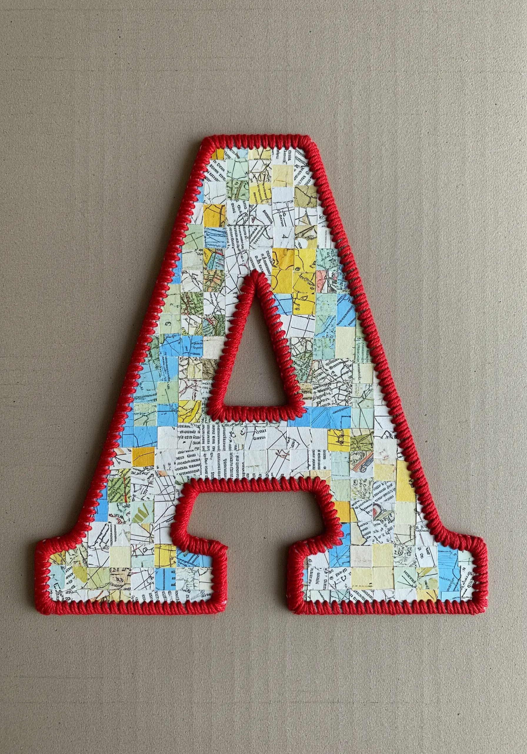 A large letter 'A' collage made from map pieces, edged with a dense red blanket stitch.