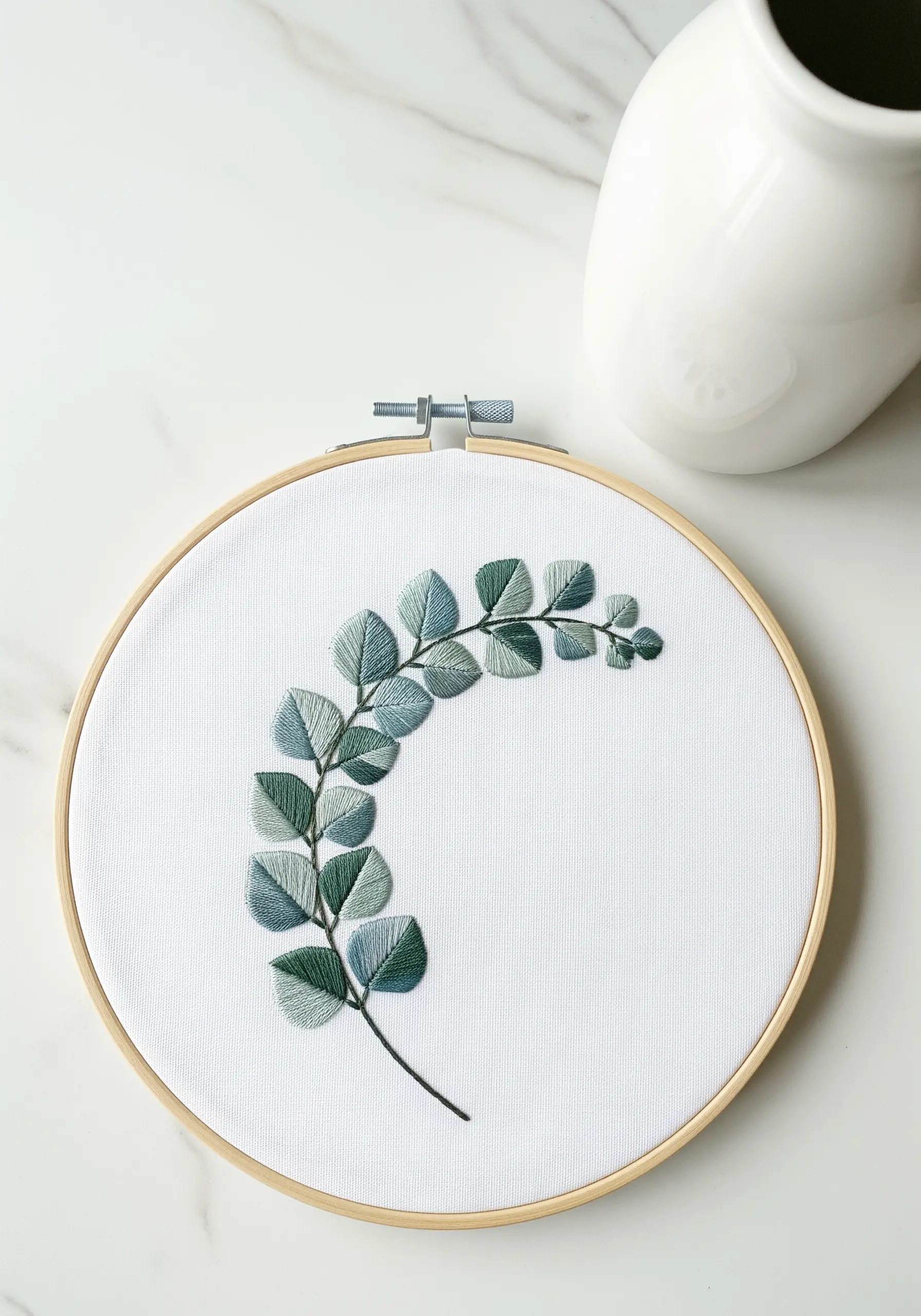 A sprig of eucalyptus with satin-stitched leaves in shades of dusty green and blue.