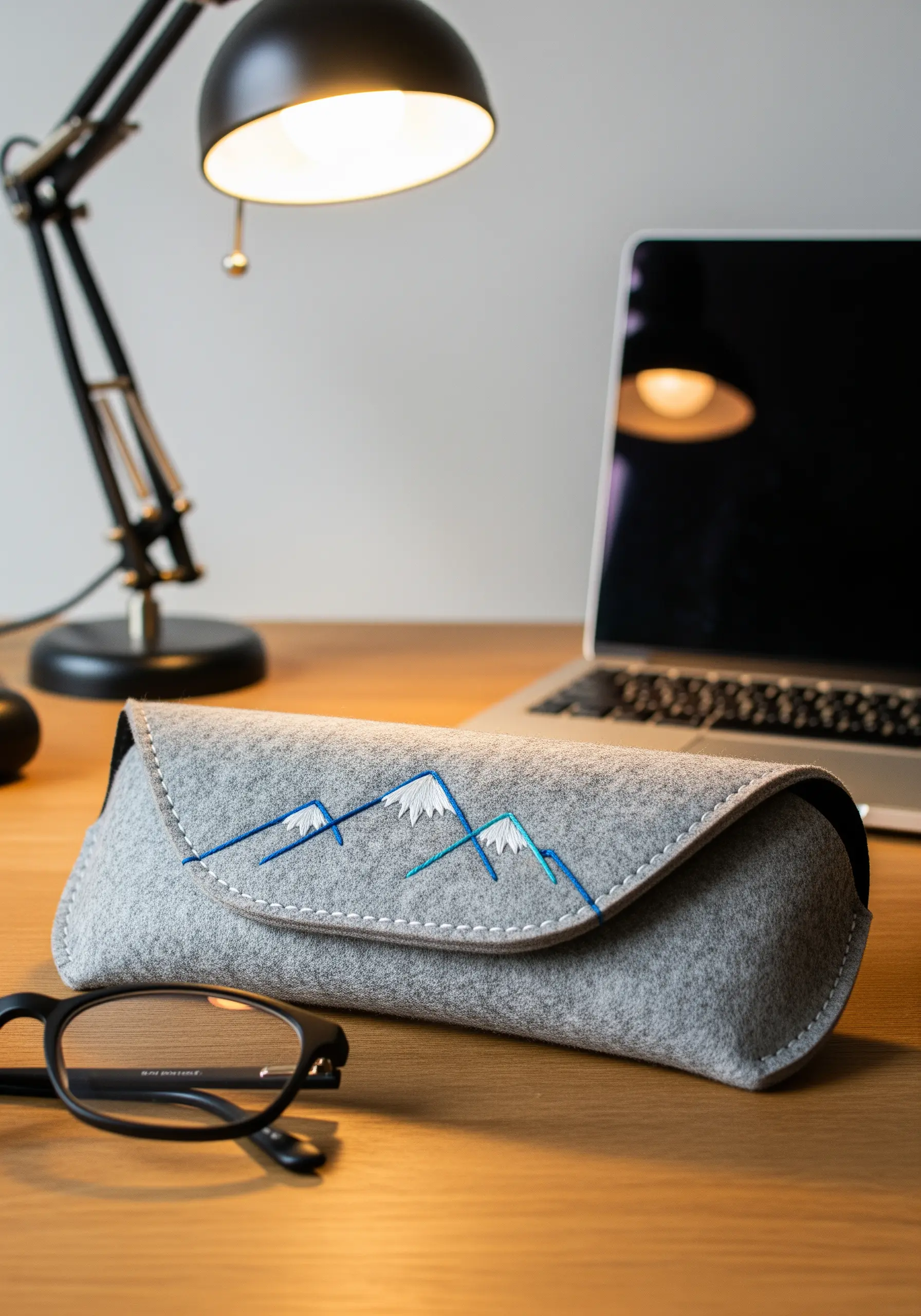 A grey felt eyeglass case with a minimalist mountain range stitched in blue and white.