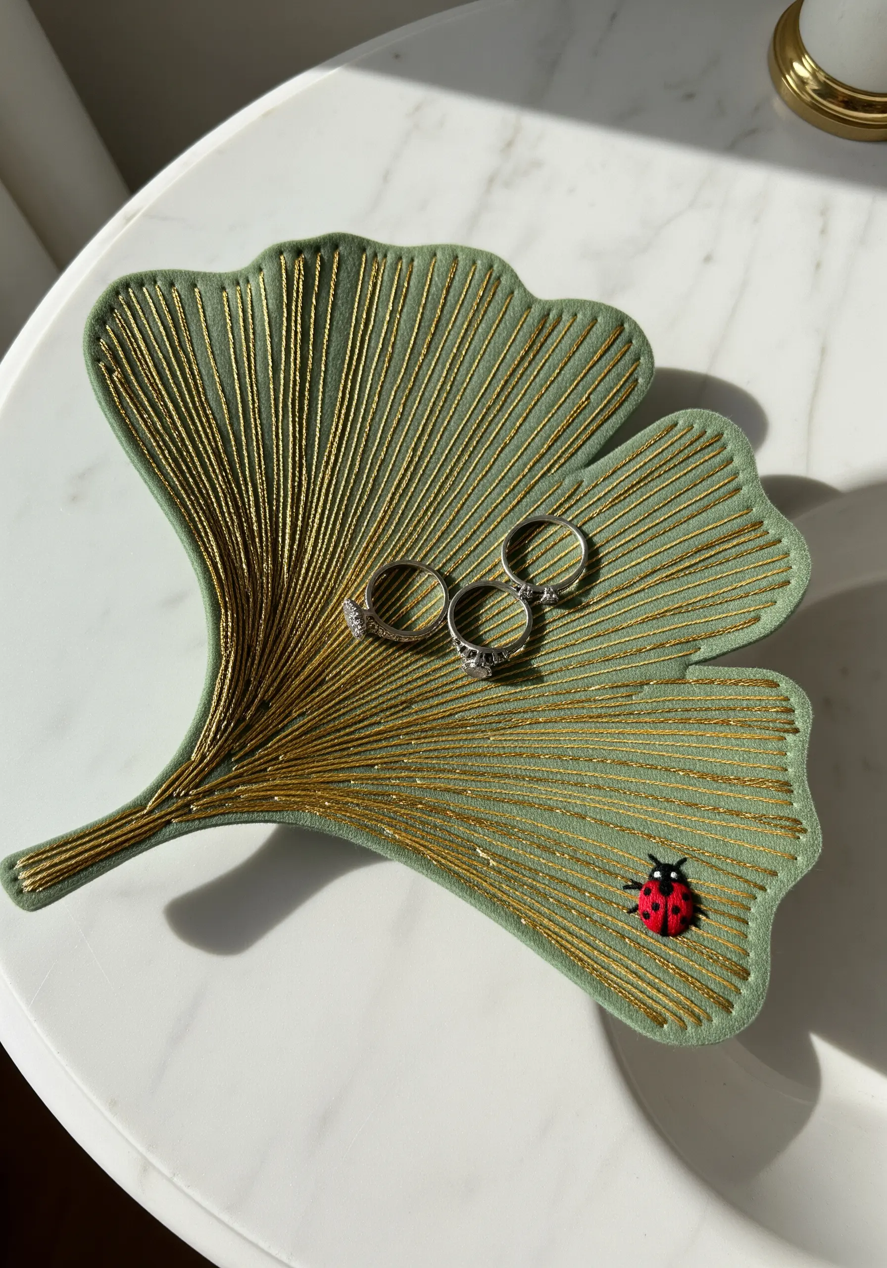 A ginkgo leaf-shaped trinket dish made of green fabric with gold threads couched on its surface.