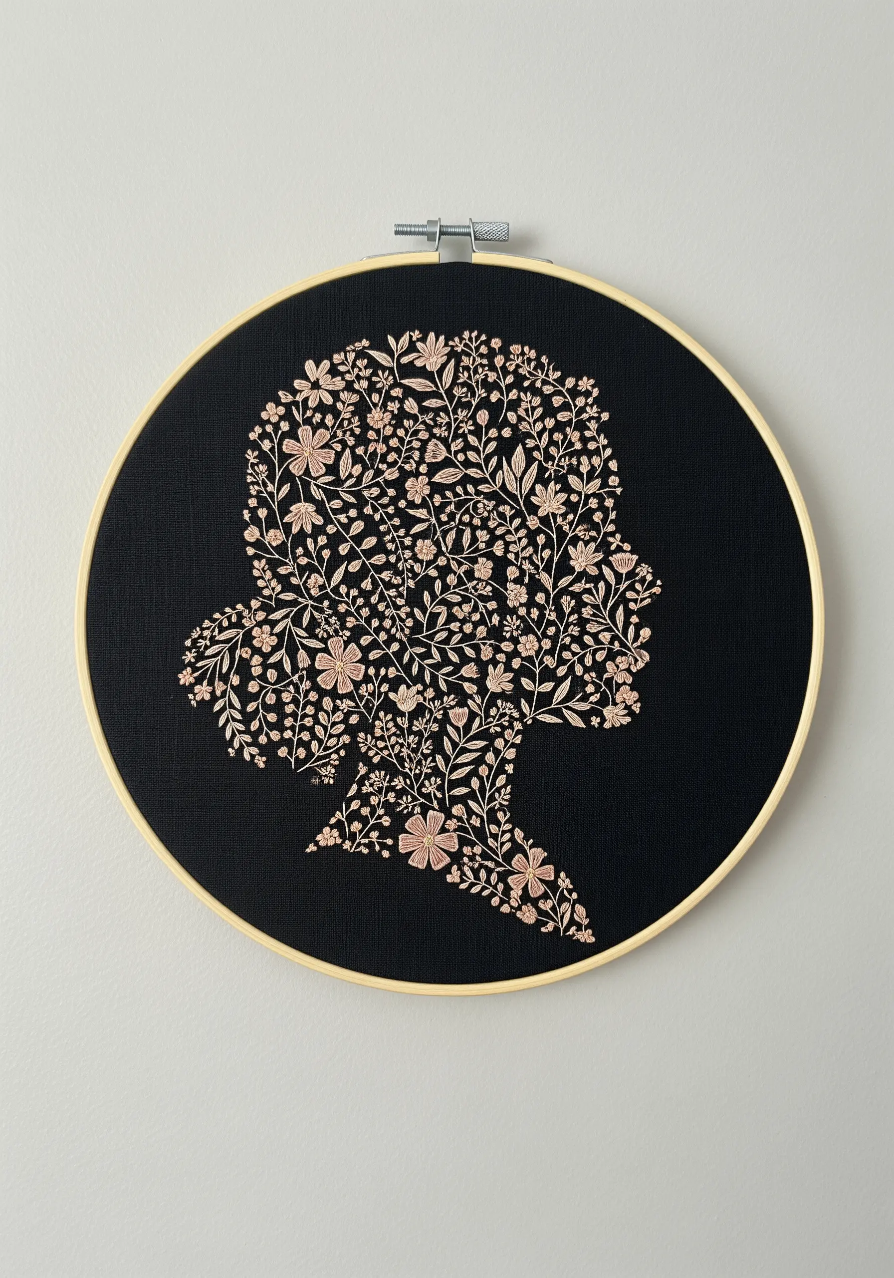 A floral silhouette of a woman's head embroidered in pink thread on black fabric