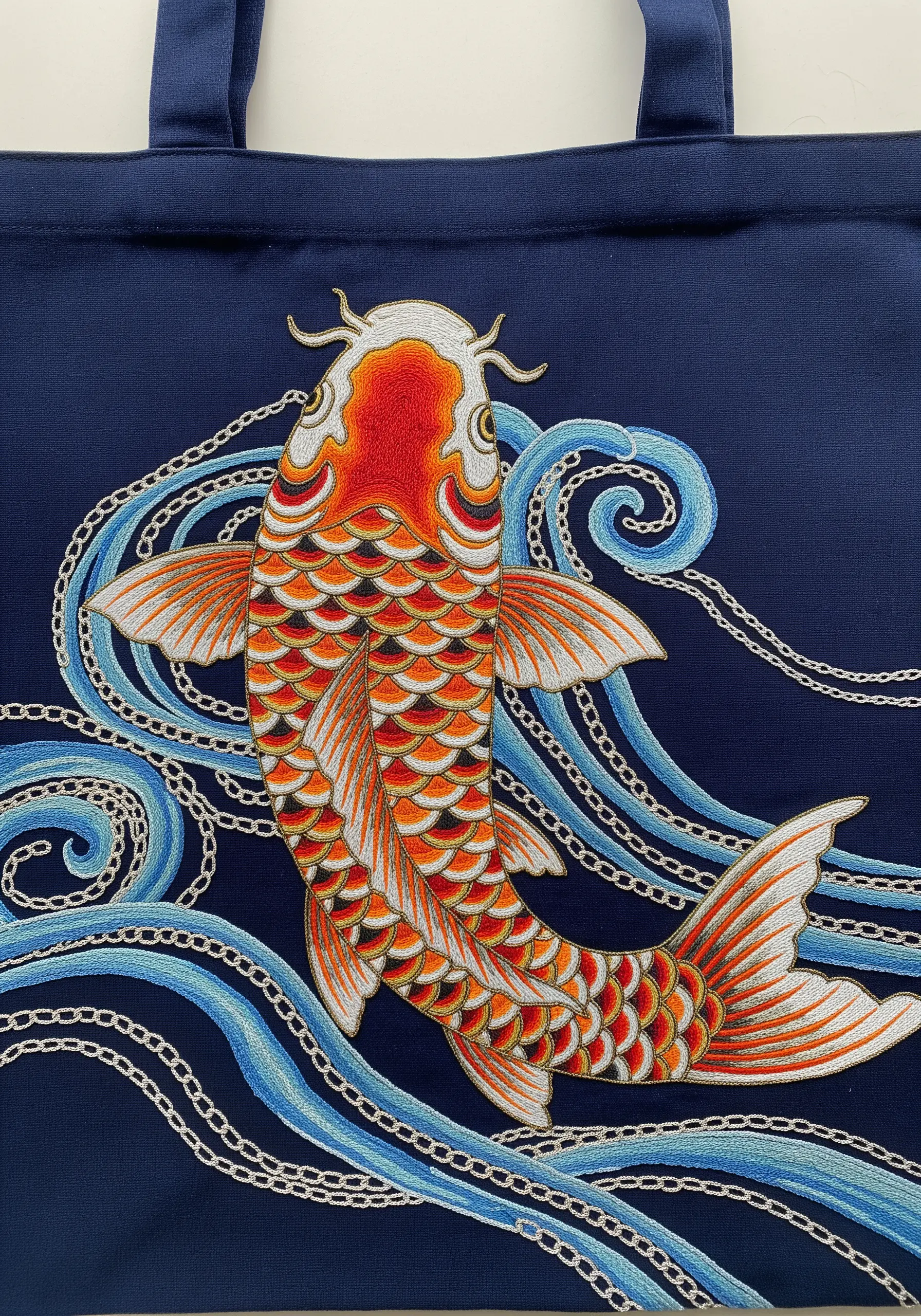 An intricately embroidered koi fish with outlined scales on a blue tote bag
