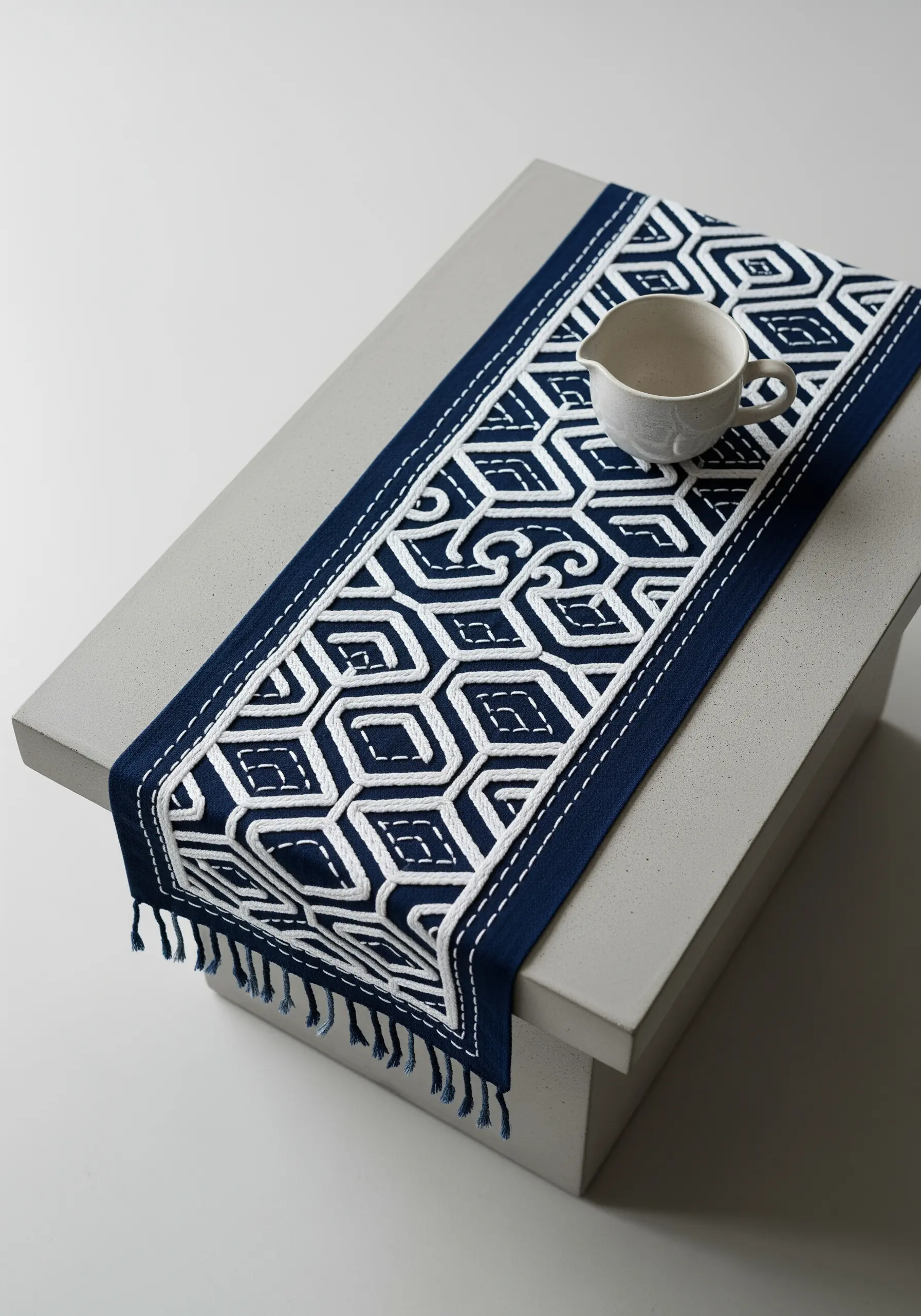 A navy blue table runner with a complex geometric pattern stitched in thick white thread.