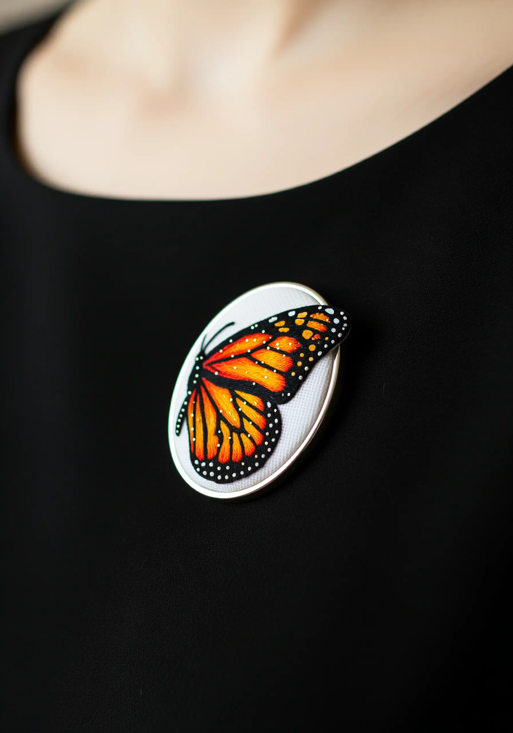 A monarch butterfly wing brooch with detailed thread painting and black outlines.