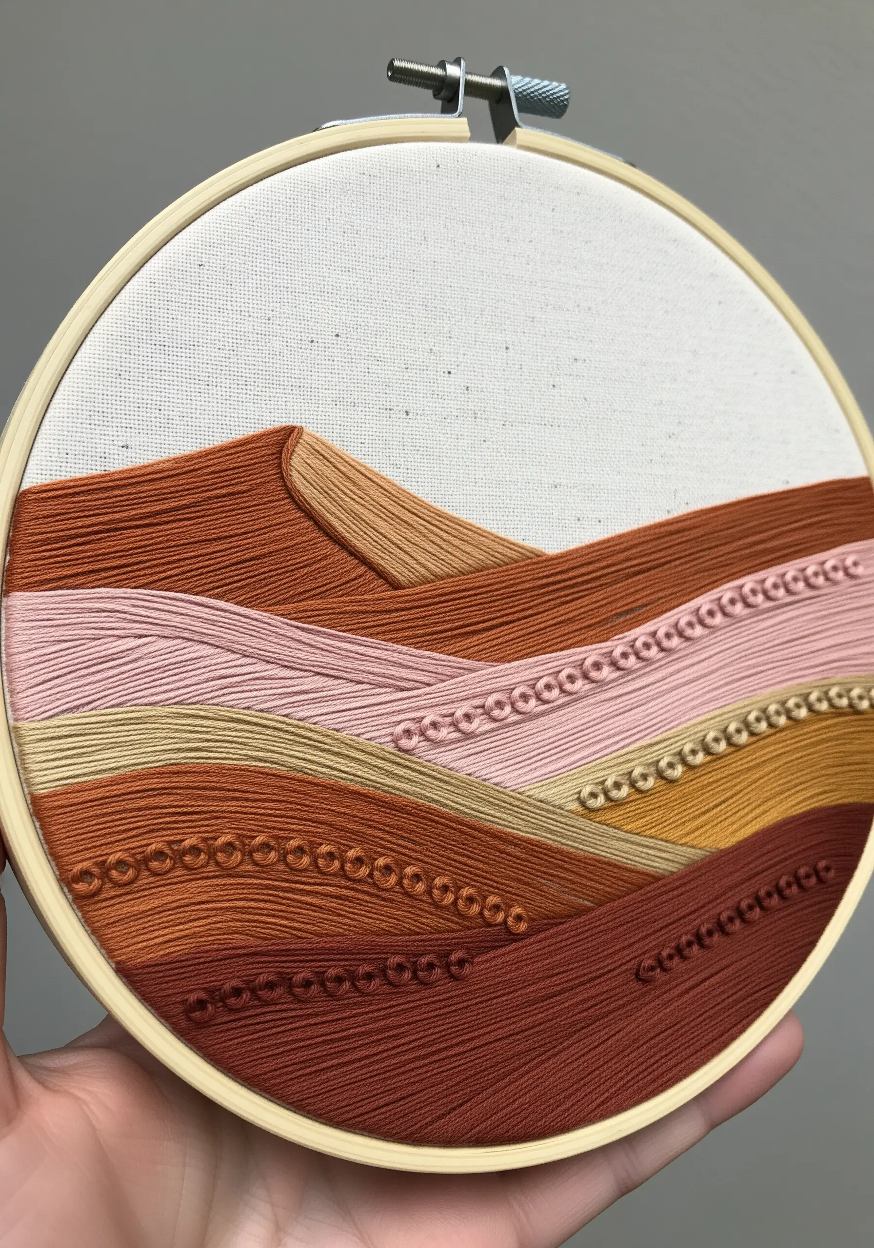 Minimalist embroidered landscape with satin-stitched hills in shades of terracotta and pink.