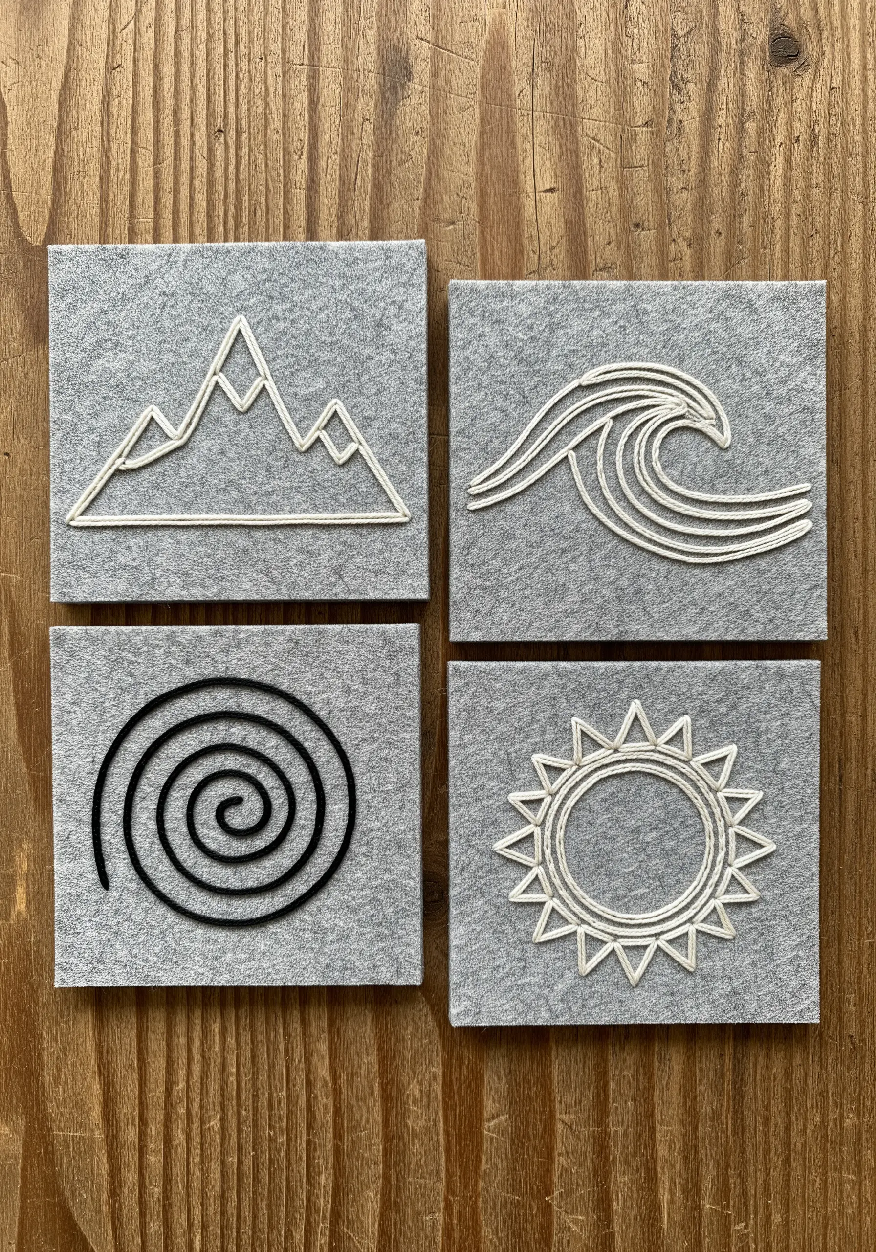 Four felt coasters with minimalist symbols stitched in raised white and black thread.