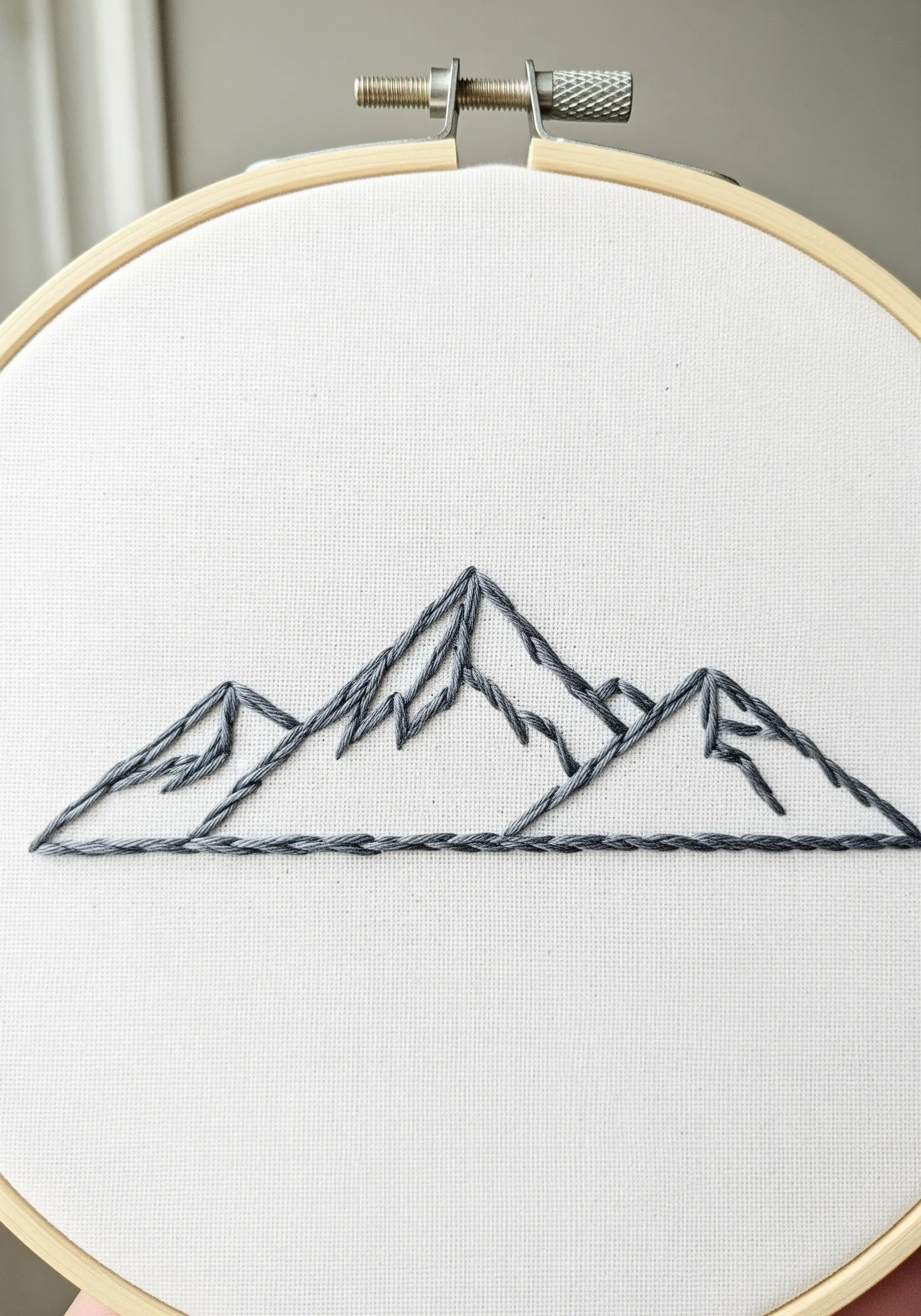 Minimalist line art embroidery of a mountain range in a hoop.