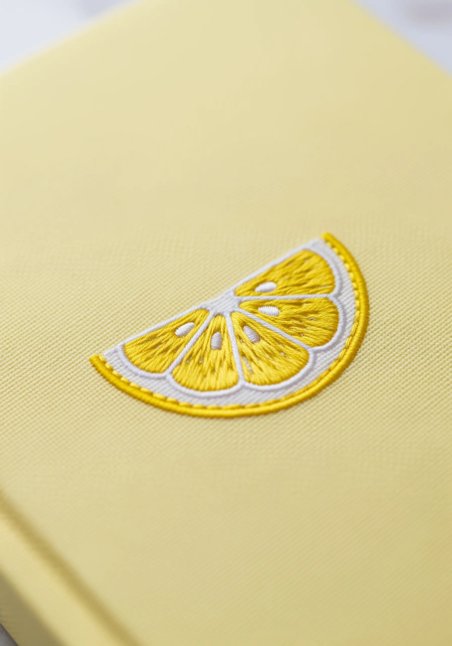 A bright embroidered lemon slice with clearly defined segments on a yellow journal.