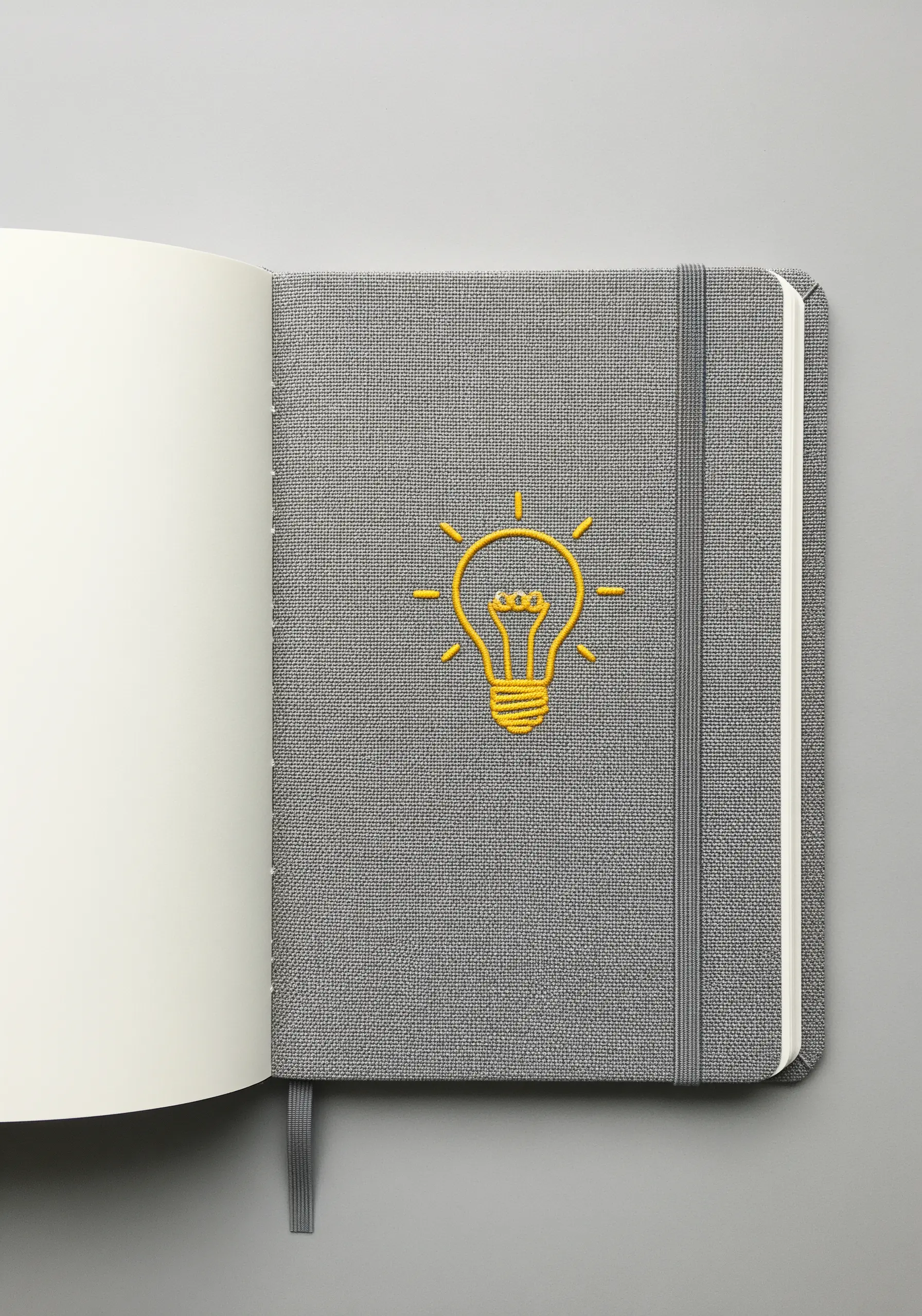 A bright yellow lightbulb outline embroidered on the cover of a grey fabric notebook.