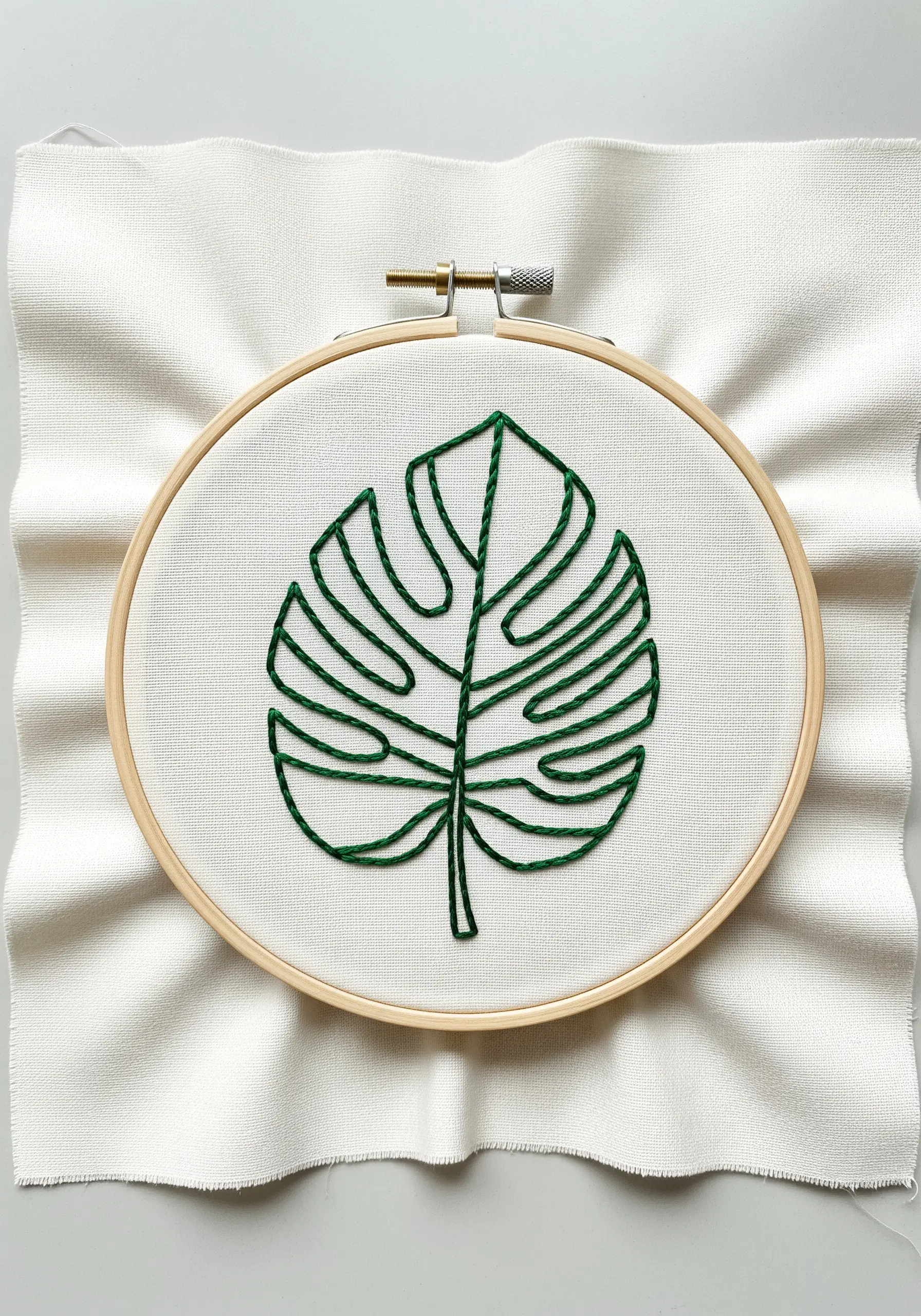 An outline of a Monstera leaf stitched in dark green thread on white fabric.