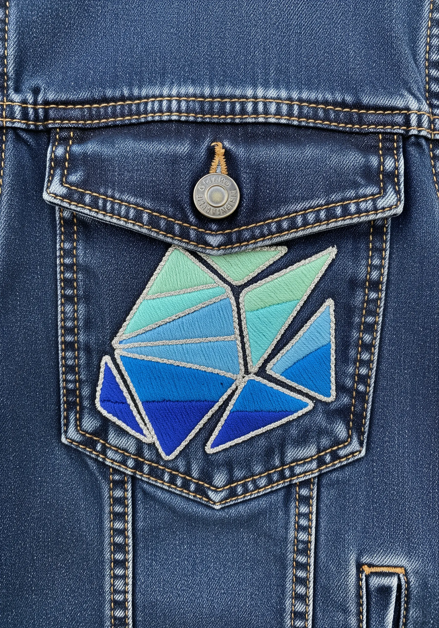 Geometric fish embroidered on a denim pocket with shades of blue and silver outlines.