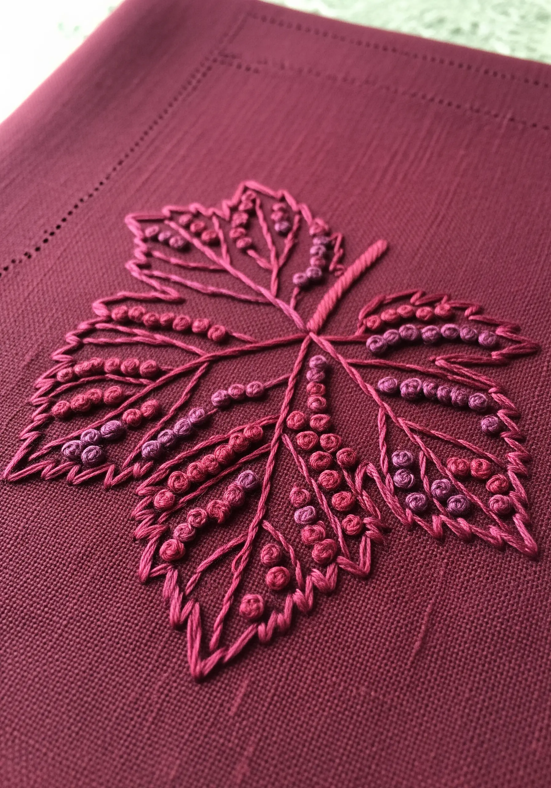 A monochrome maple leaf where veins are created by negative space between French knot clusters.
