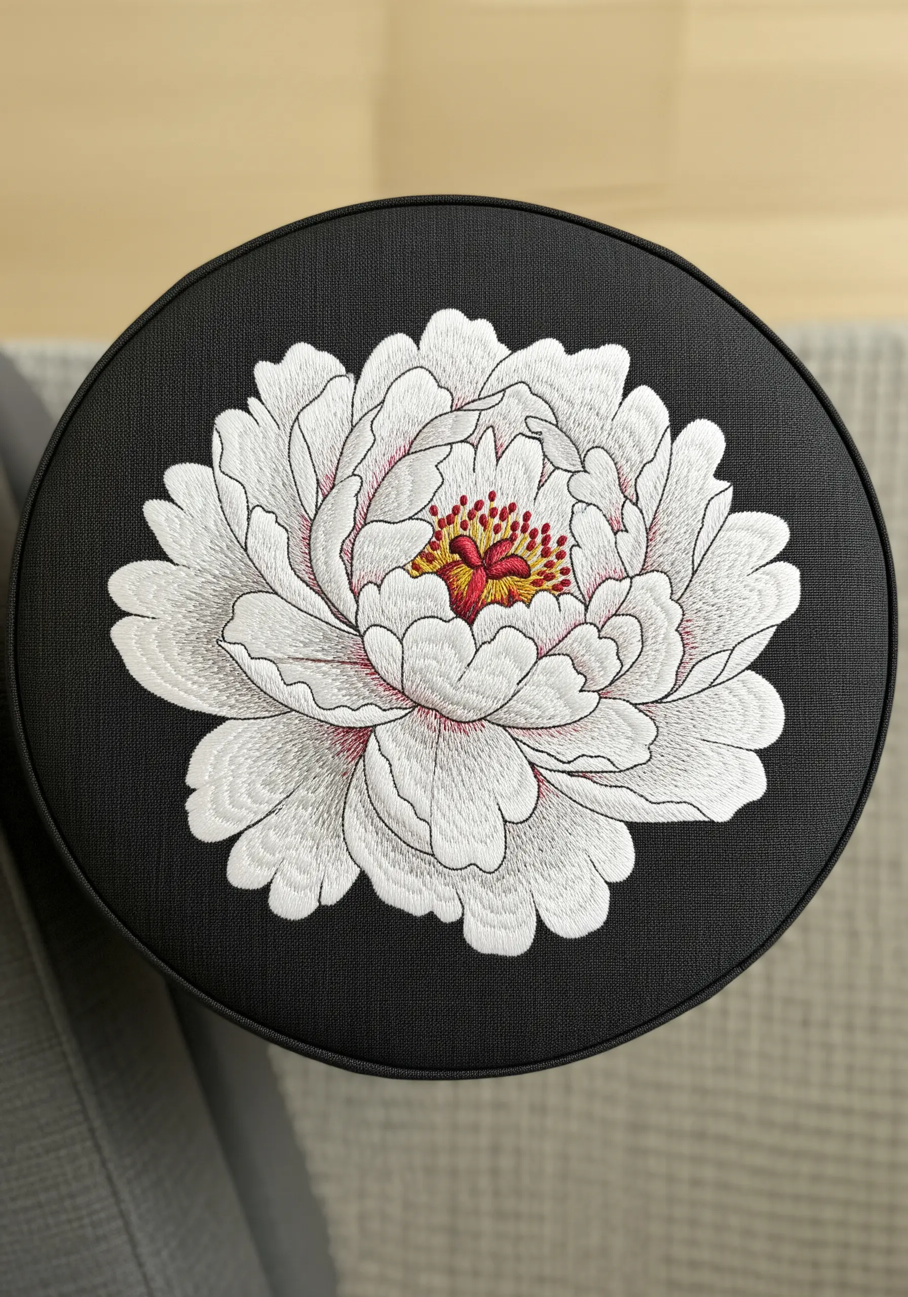 A white peony with grey shading and a red center on a black round cushion.
