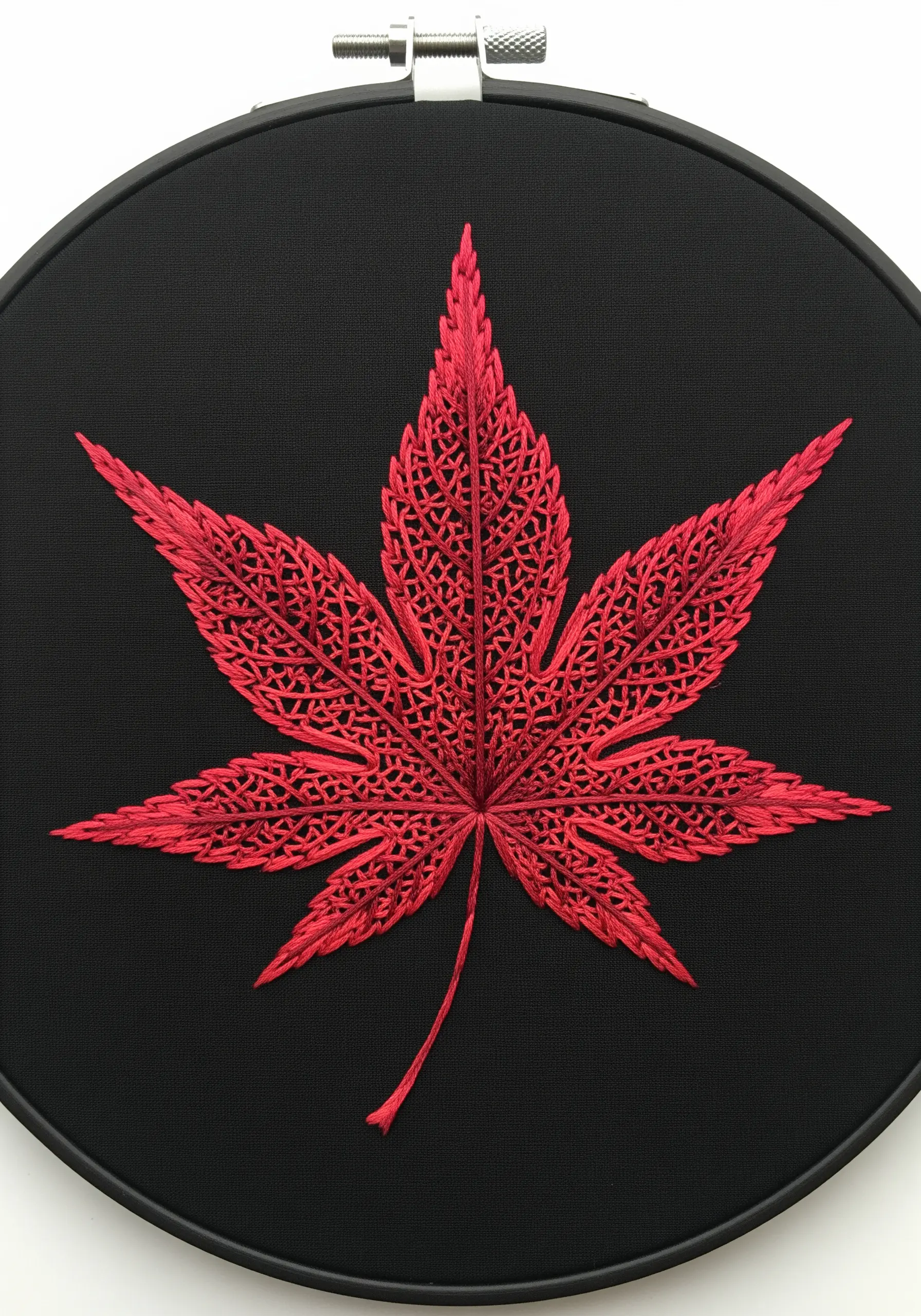 A red Japanese maple leaf created with intricate cutwork embroidery on black fabric.