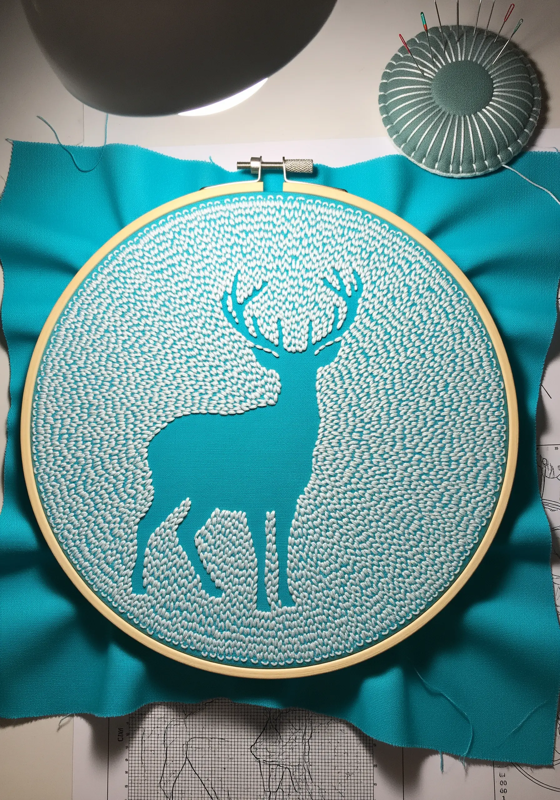 A deer silhouette created with negative space against white seed stitches on teal fabric.