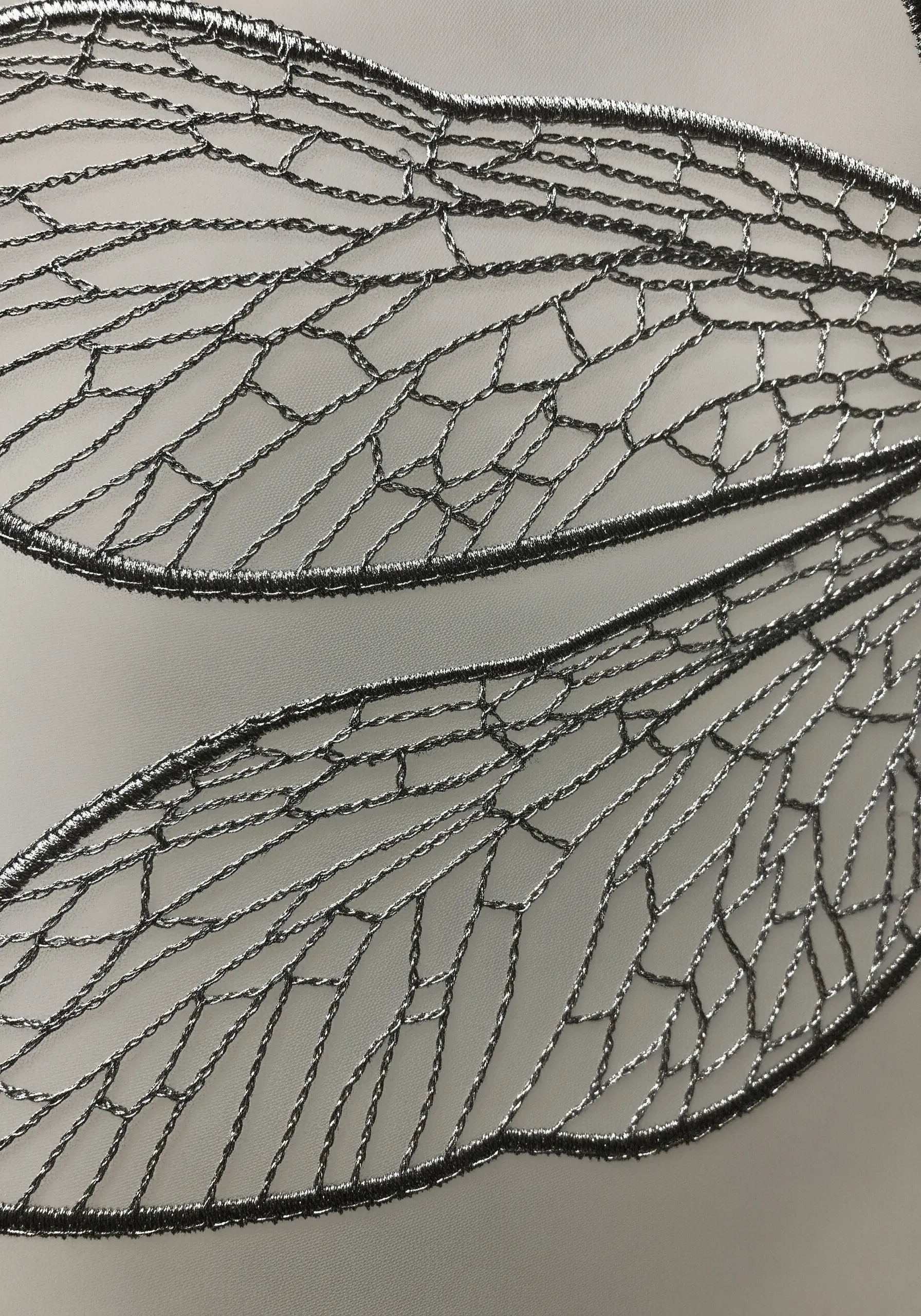 Close-up of embroidered dragonfly wings using silver metallic thread to create intricate vein patterns.