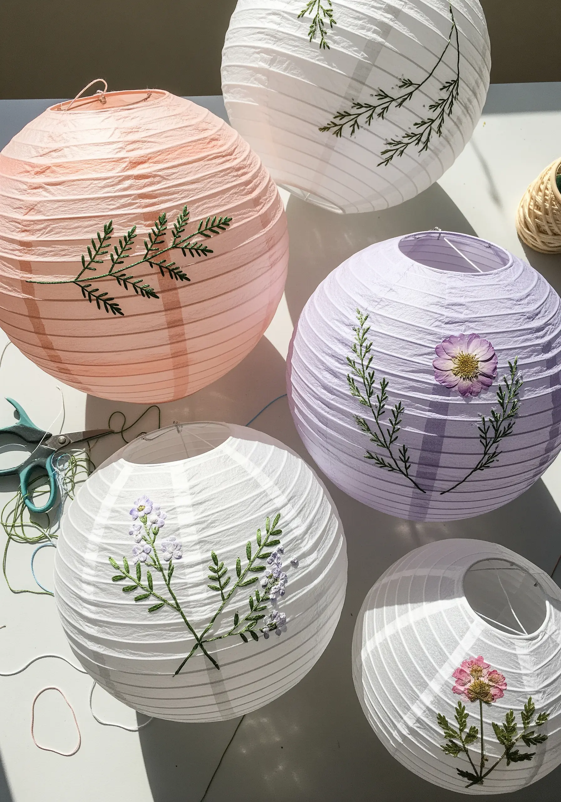 Embroidered ferns and pressed flowers on pink, purple, and white paper lanterns.