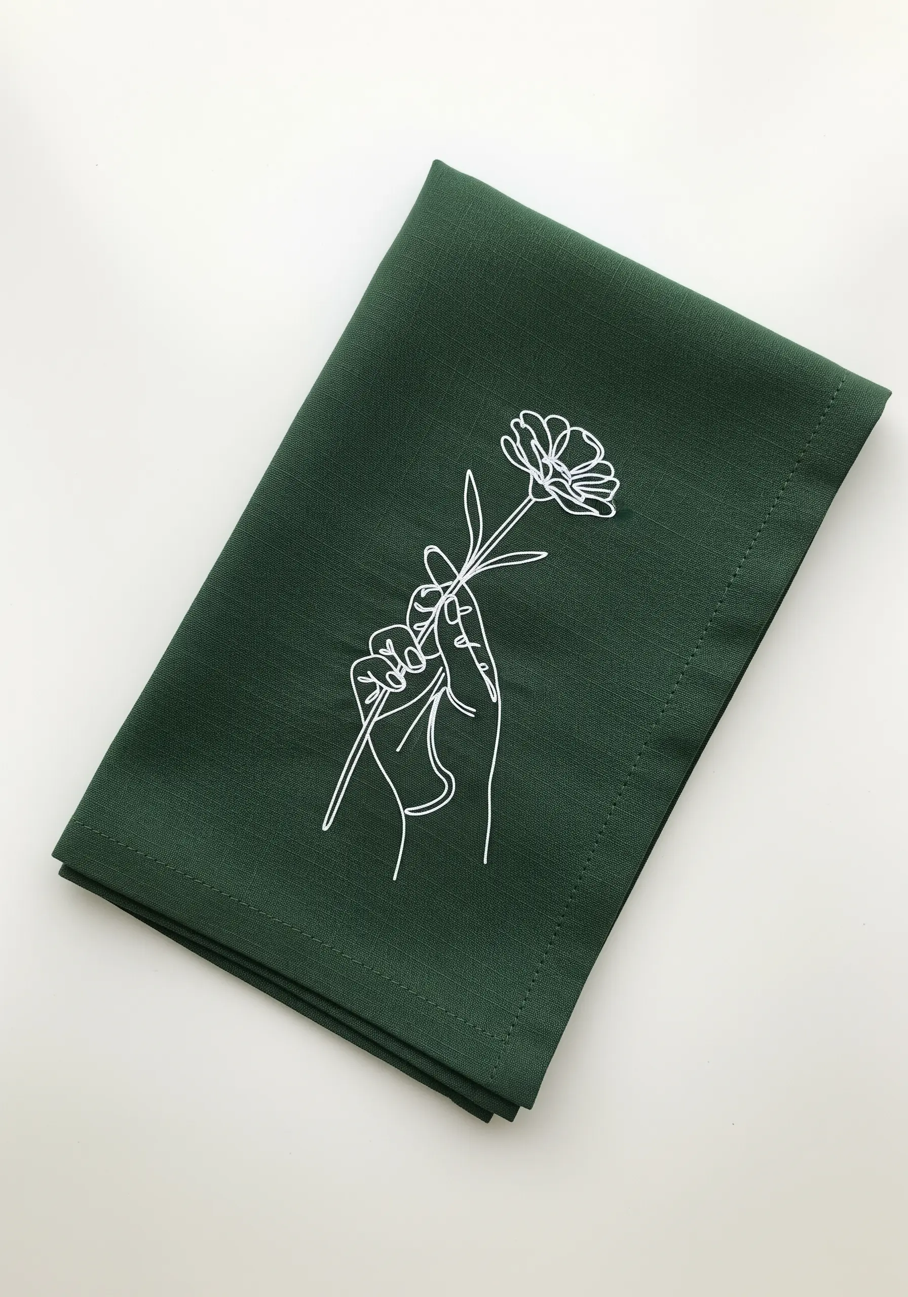 White line art of a hand holding a flower, stitched on dark green linen.