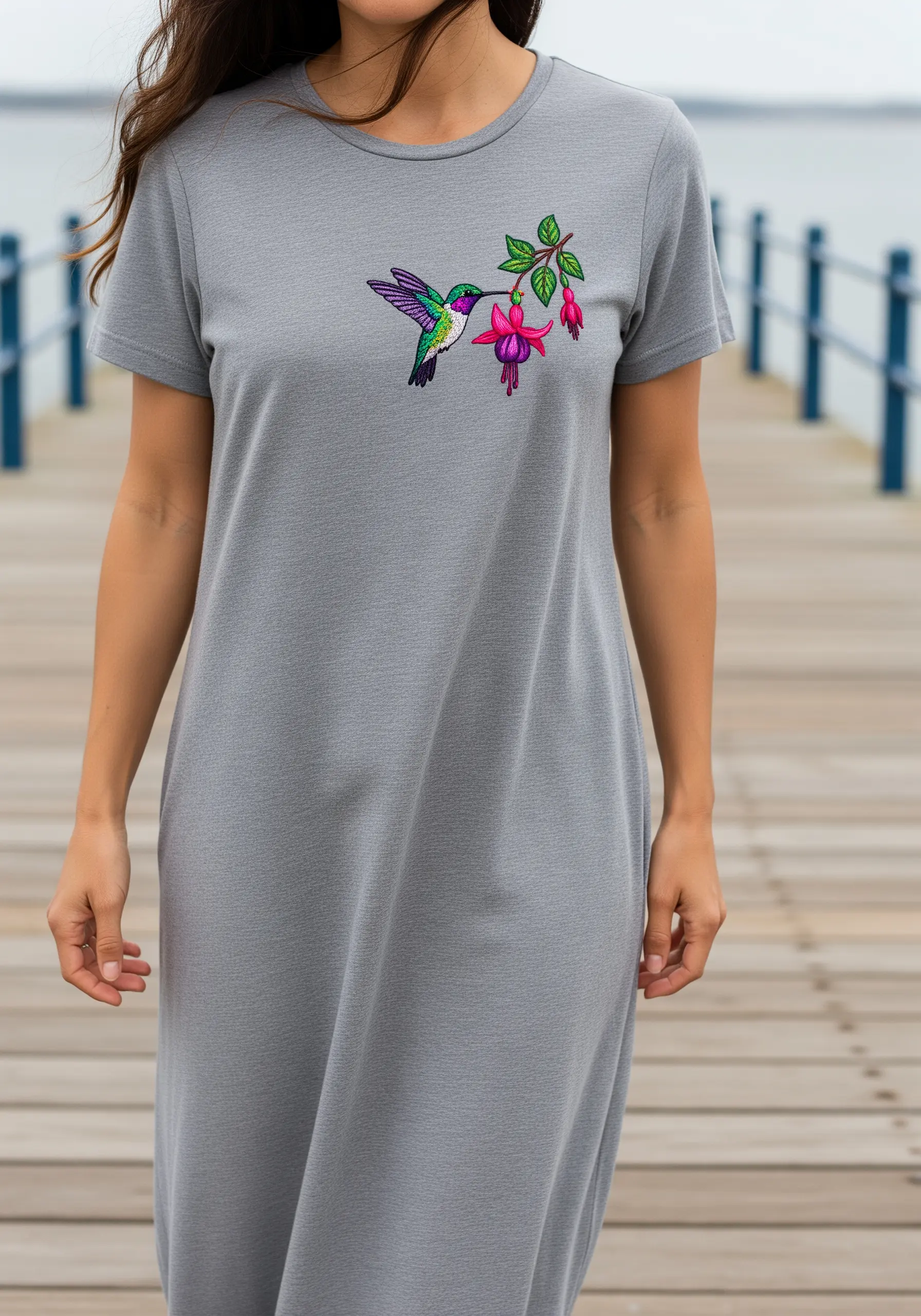A small, detailed embroidery of a hummingbird and fuchsia flower on a gray t-shirt dress.